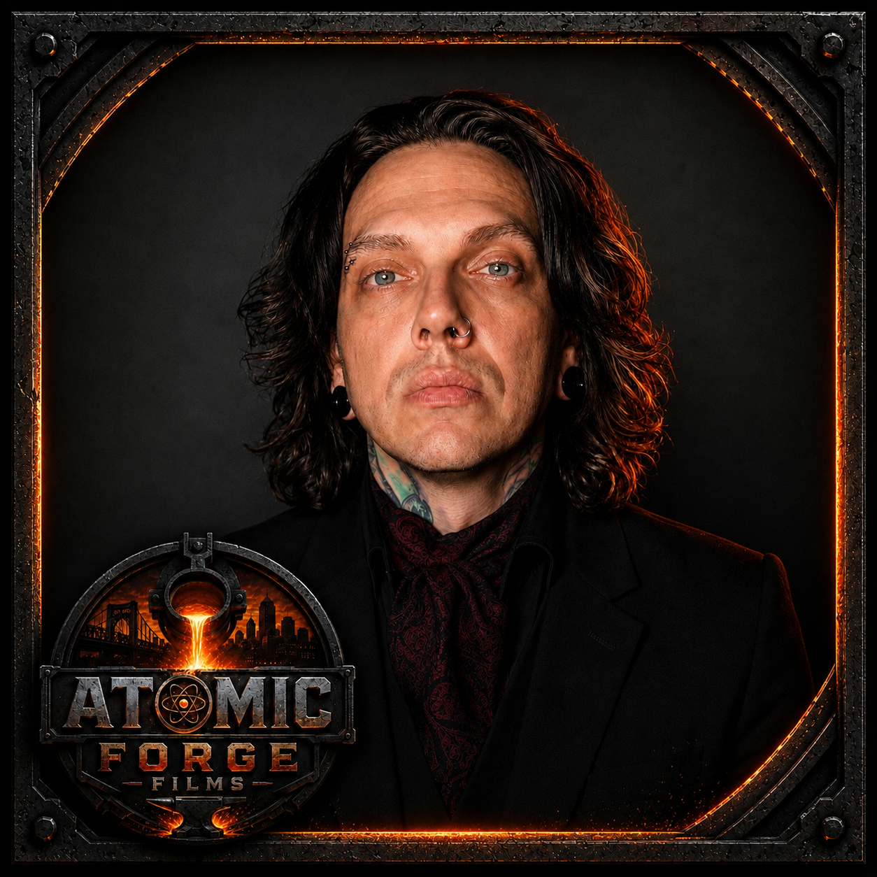 Portrait of a man with long wavy black hair, piercings including a septum ring and earrings, wearing a dark suit and red patterned scarf, set against a dark background with a fiery orange and black border. The bottom left corner features a logo for "Atomic Forge Films" with a city skyline and bridge silhouette.