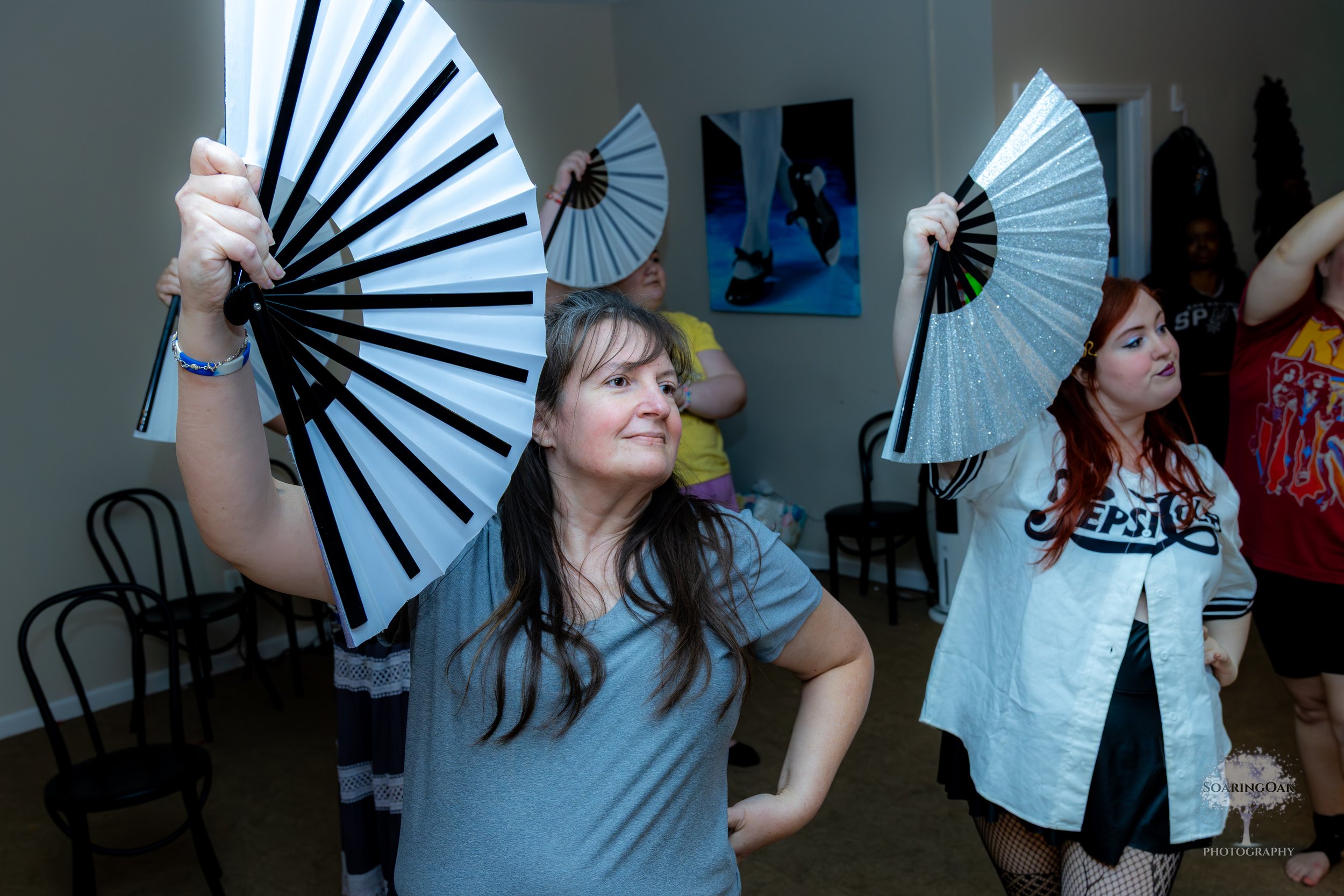 People dancing and holding fans in a room, dressed in casual and festive clothing.
