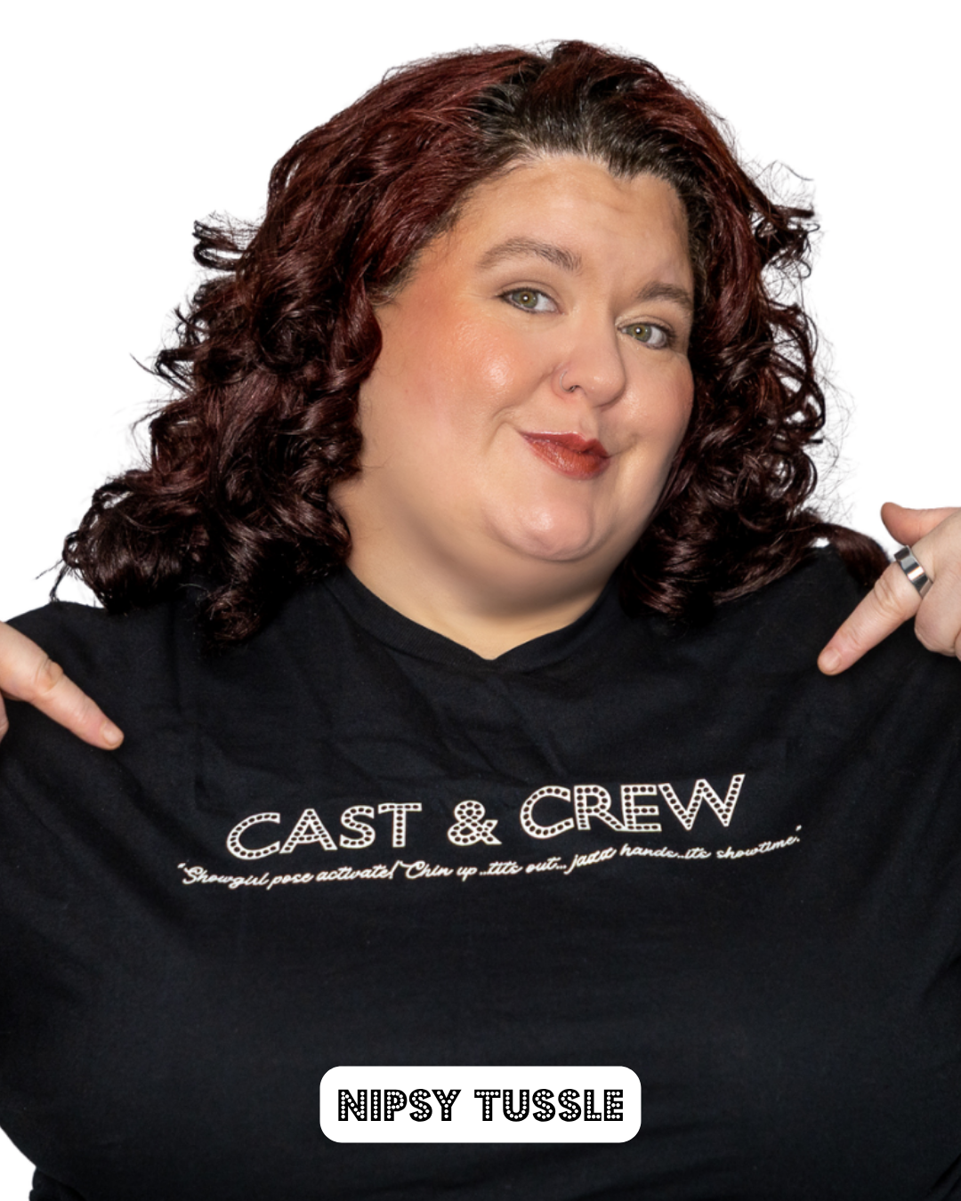 Woman with curly dark red hair pointing to her black t-shirt that says "CAST & CREW" and below that, "NIPSY TUSSLE" in bold letters.