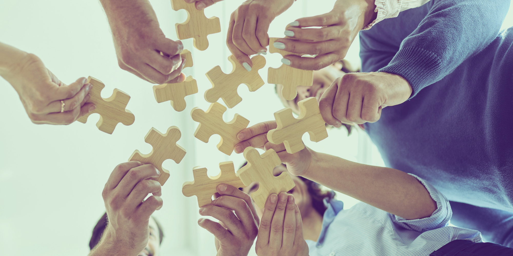 Multiple people working together to assemble a puzzle of large wooden pieces, symbolizing teamwork.