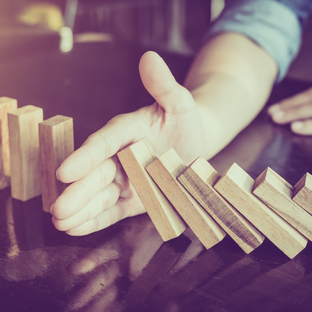 Person's hand knocking down wooden dominoes on a dark surface.