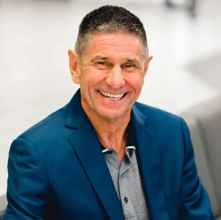 A smiling middle-aged man wearing a blue blazer and gray shirt.