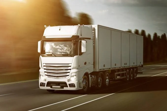 A white semi-truck driving on an open highway at sunset.