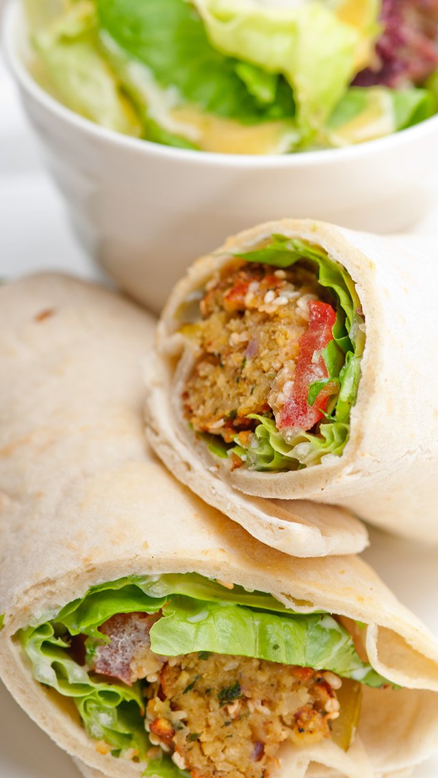 Three wraps filled with seasoned ground meat, lettuce, and fresh vegetables, served alongside a bowl of salad with leafy greens.