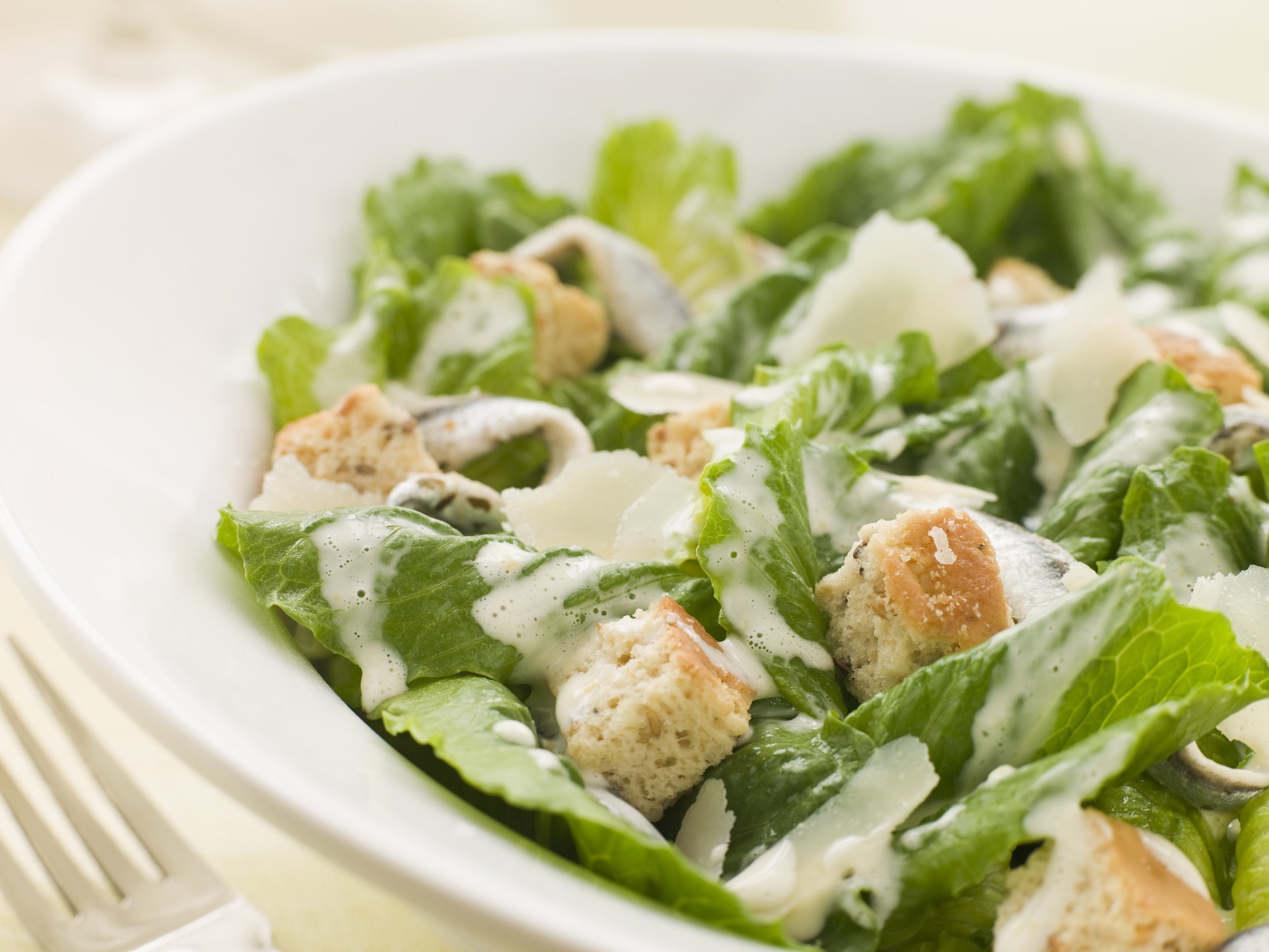 A close-up of a Caesar salad in a white bowl, topped with grated cheese and croutons.