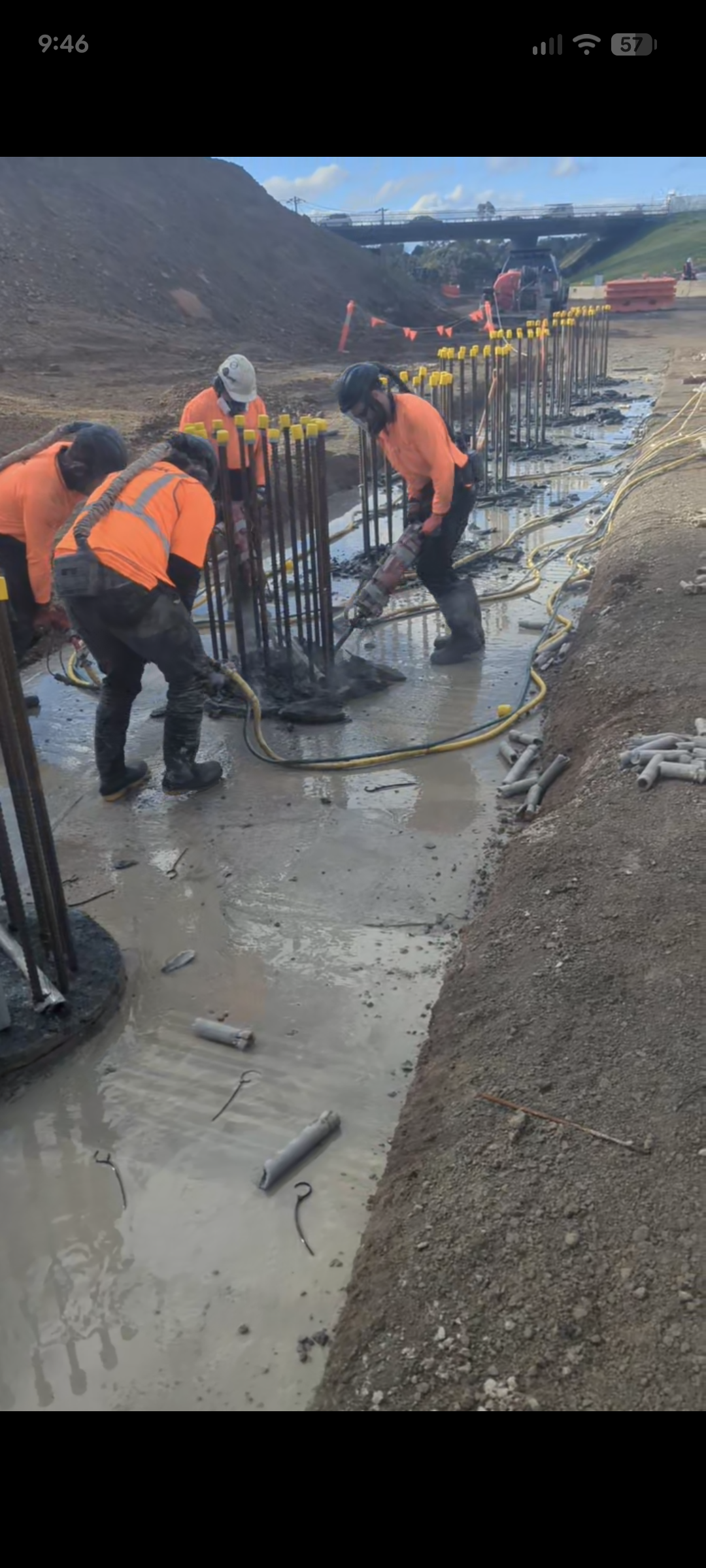 Workers in orange safety vests and helmets pouring and spreading concrete on a construction site foundation with rebar.