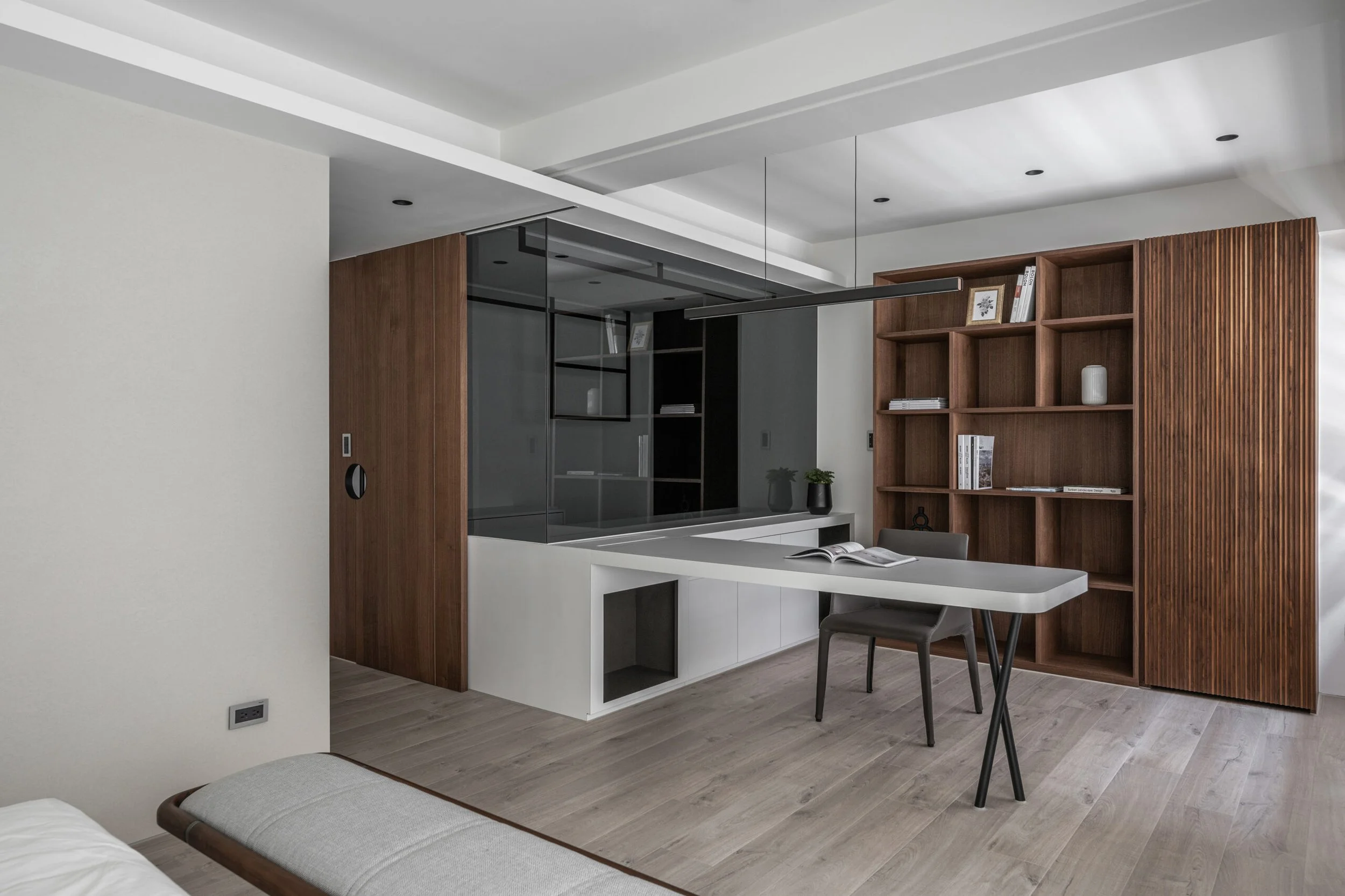 Modern living space with a white kitchen counter, a dining table, and a wooden bookshelf with books and decorative items.