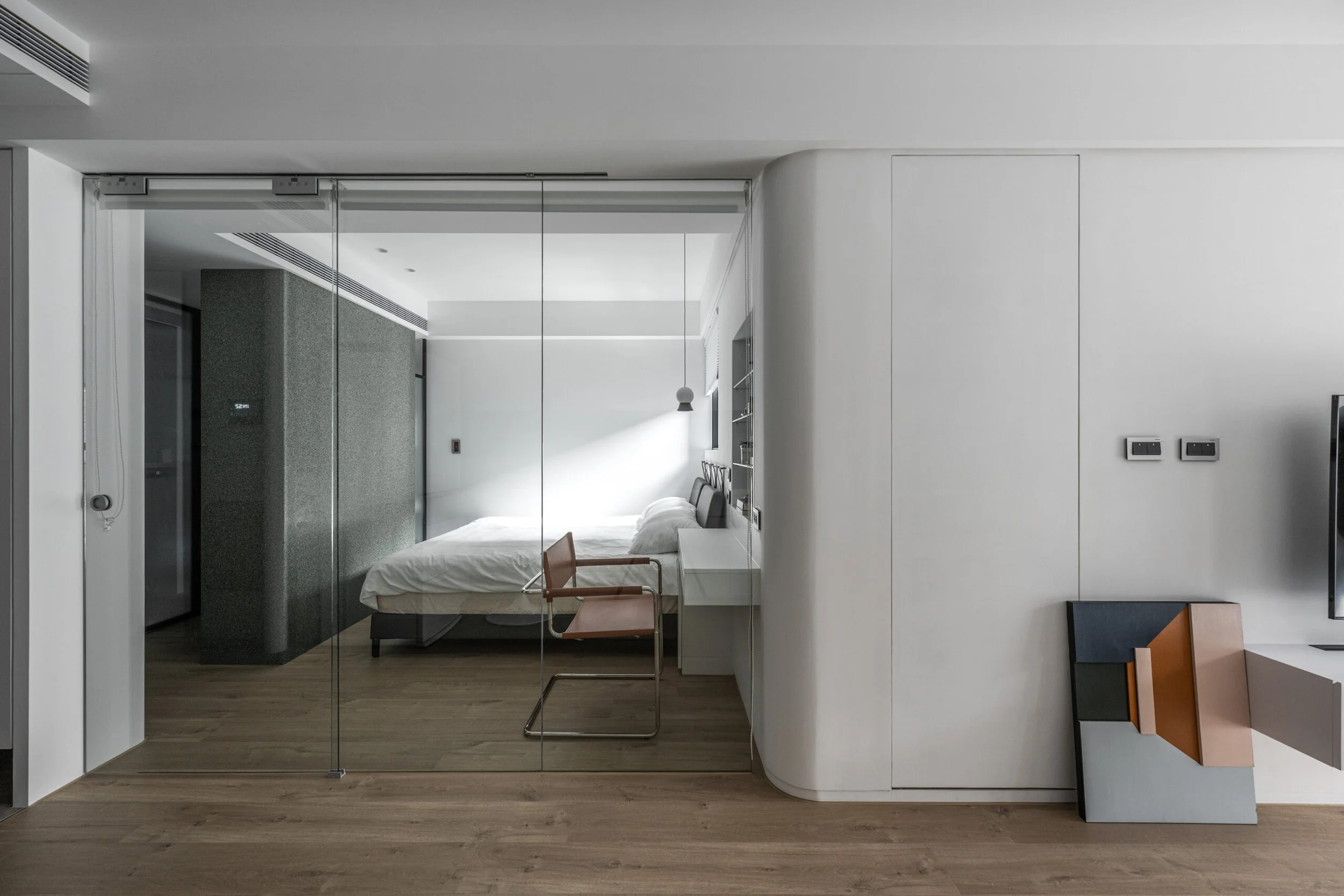 Modern hotel room with a bed, glass wall, and minimalistic furniture.