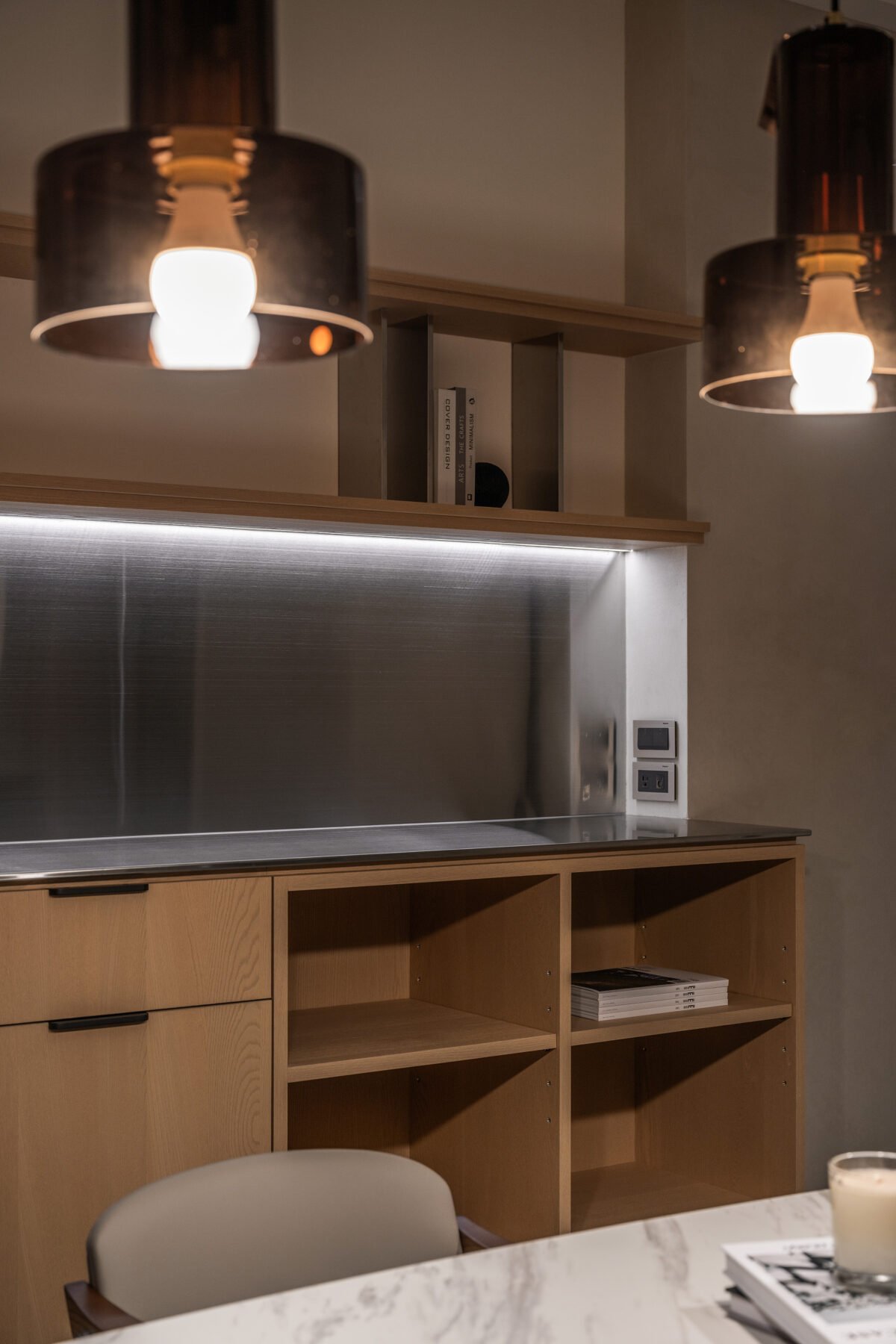 Close-up of modern kitchen with hanging black pendant lights, wooden cabinets, and a marble countertop.