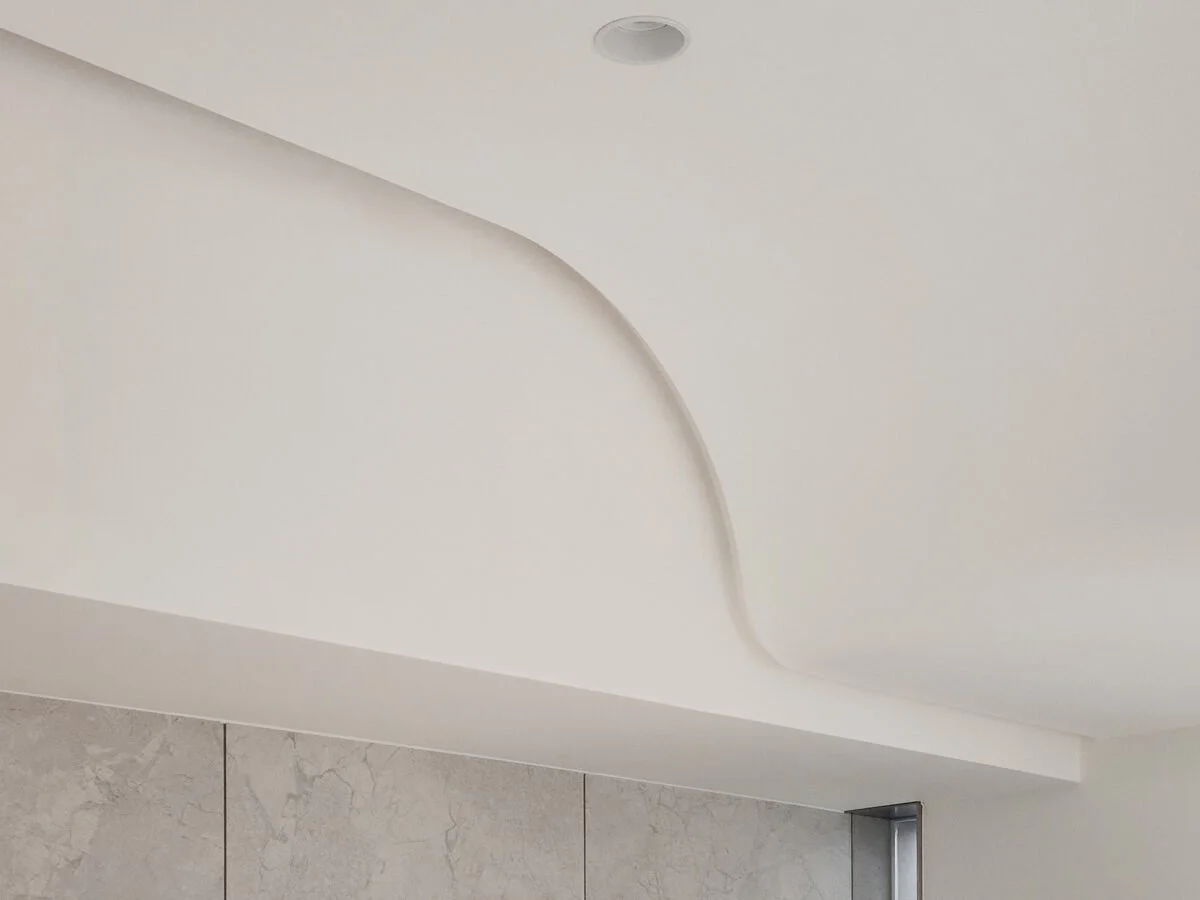 Close-up view of a white ceiling with a curved design element and a small round recessed light fixture.