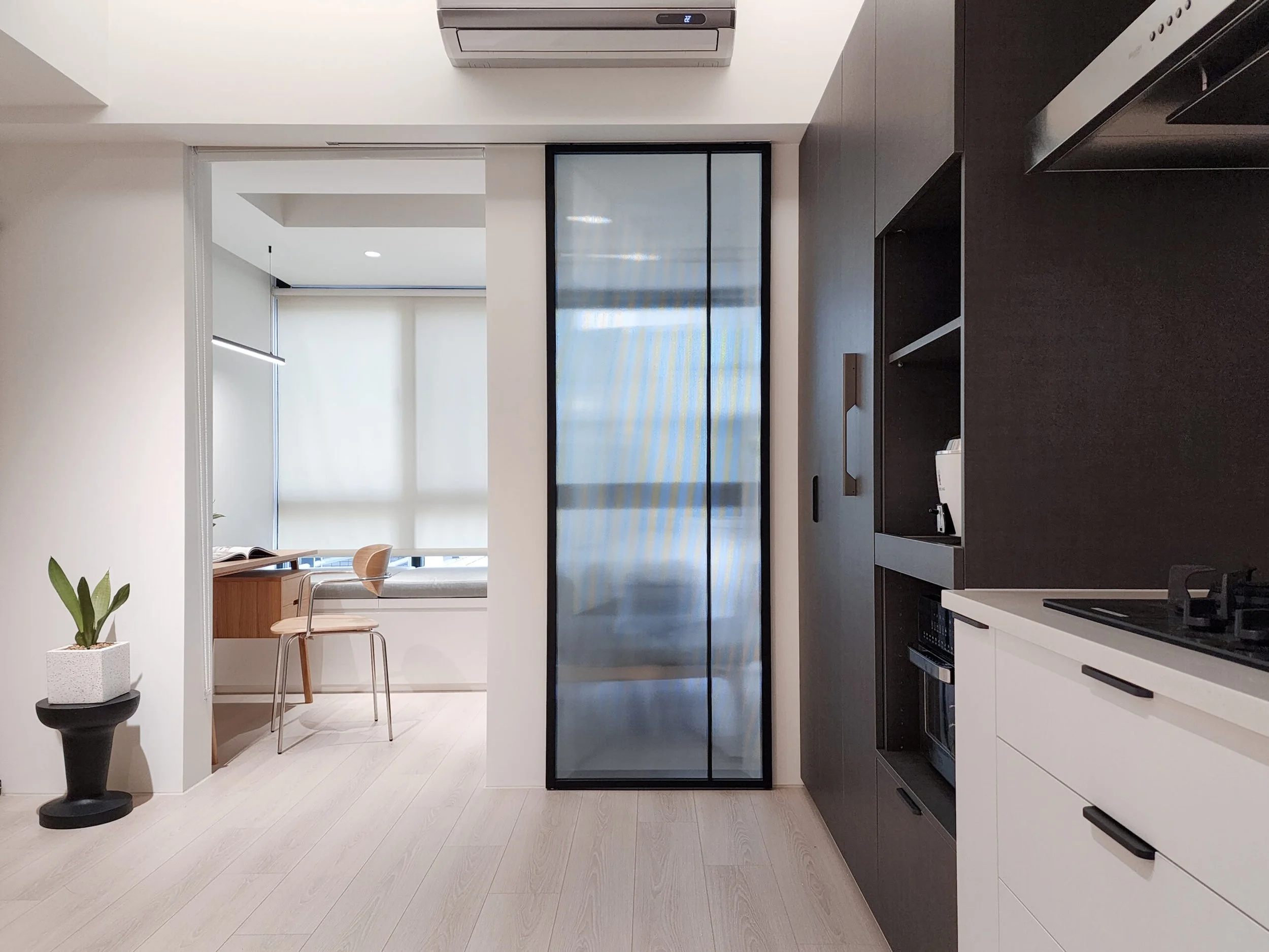Modern kitchen with black and white cabinets, a black countertop, a stove, and a sliding glass door leading to a balcony or patio. There is a potted plant with green leaves on a black stand in the foreground.