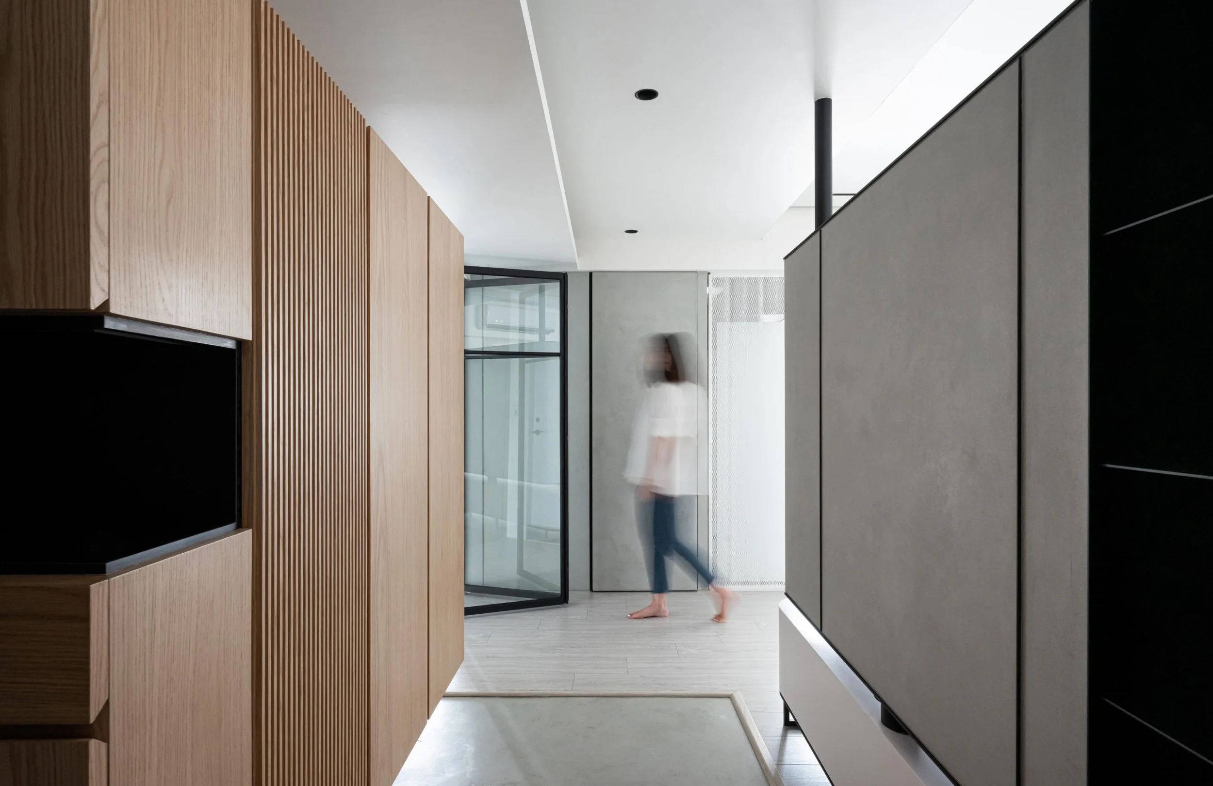 Modern interior space with wooden panels, glass doors, and a blurred person walking.