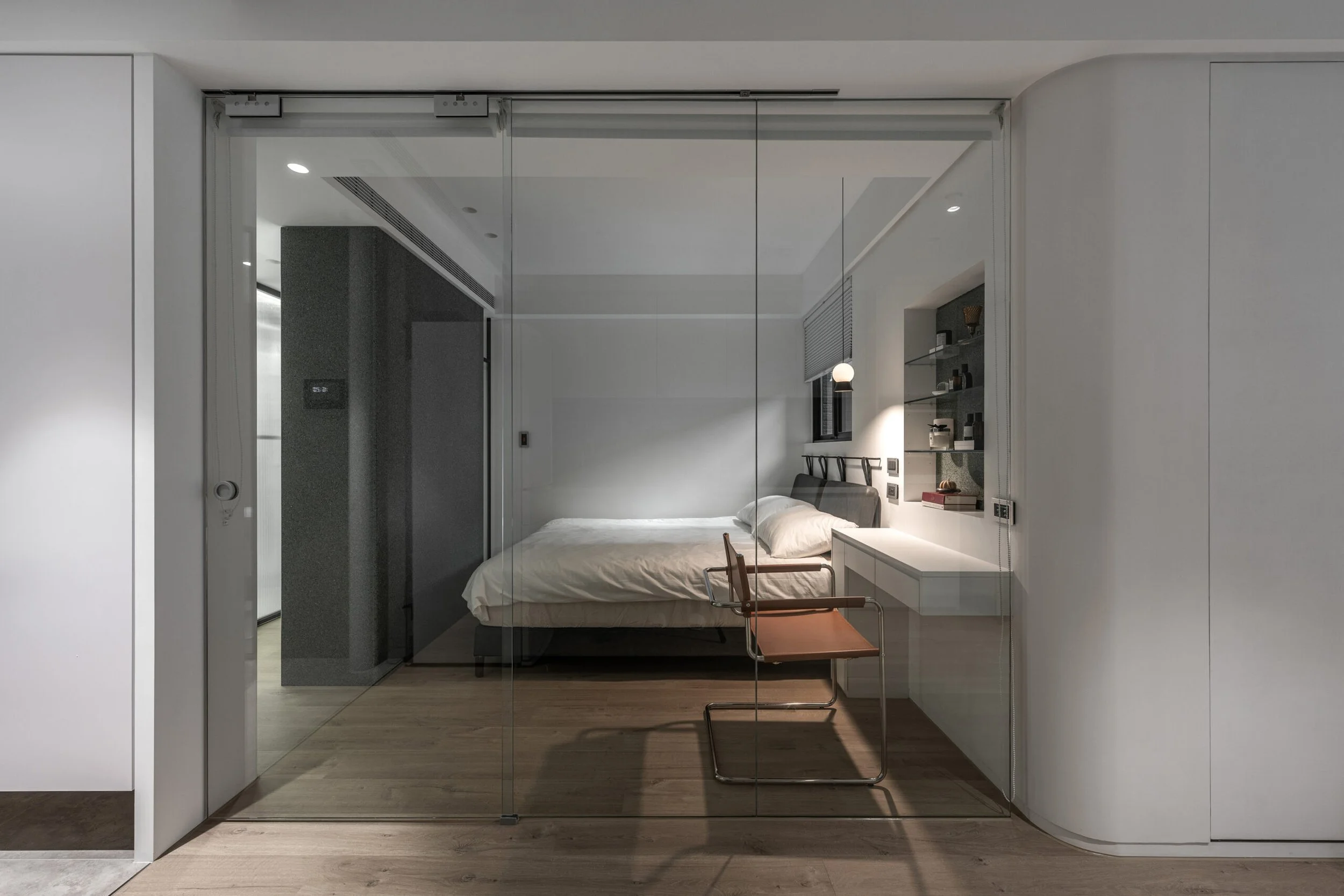 Modern bedroom with glass sliding doors, a bed with white bedding, and built-in shelves with decor.