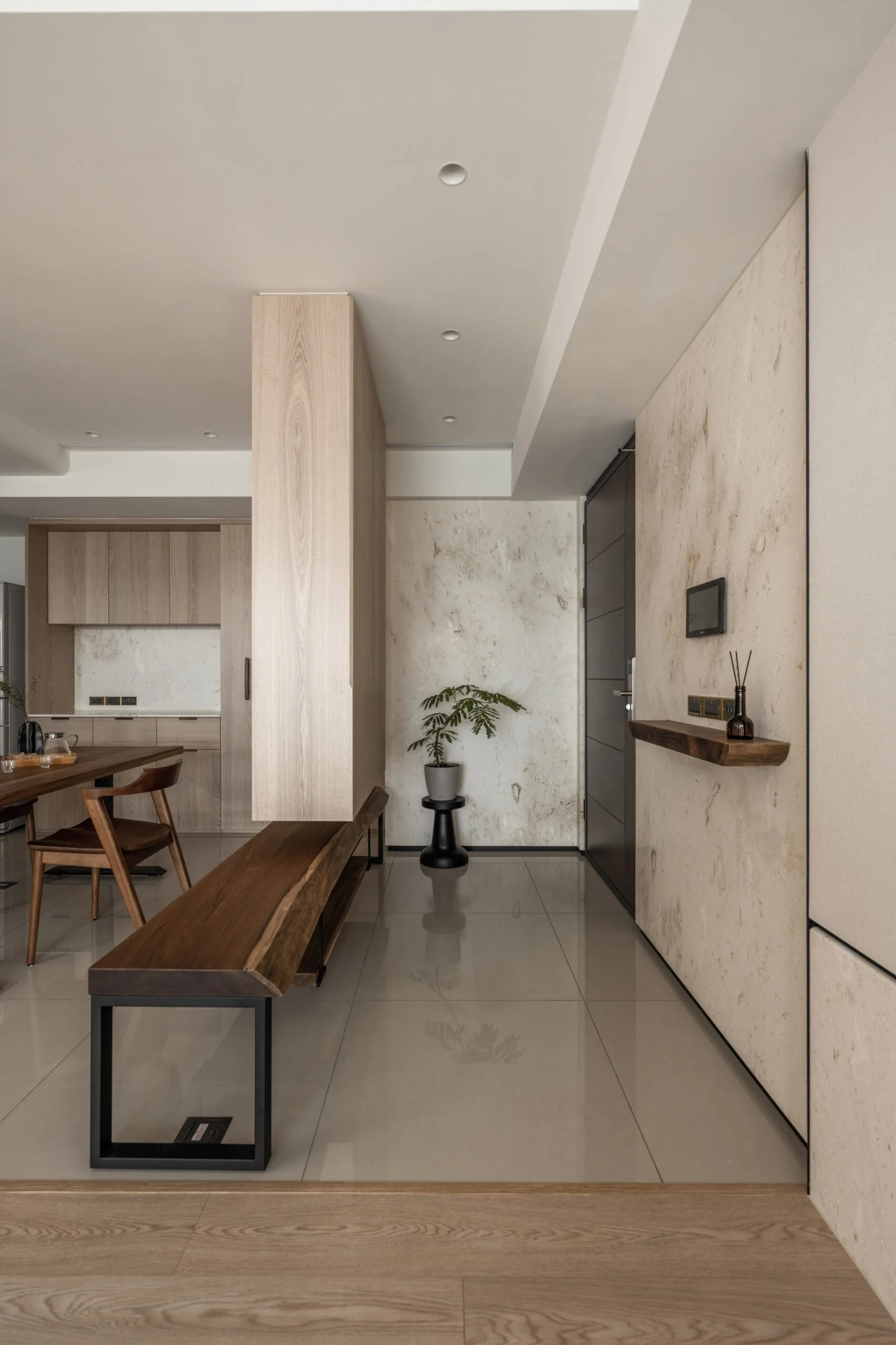 Modern interior space featuring a wooden bench with black metal legs, a potted plant, a grey wall with black trim, and kitchen cabinetry in the background.