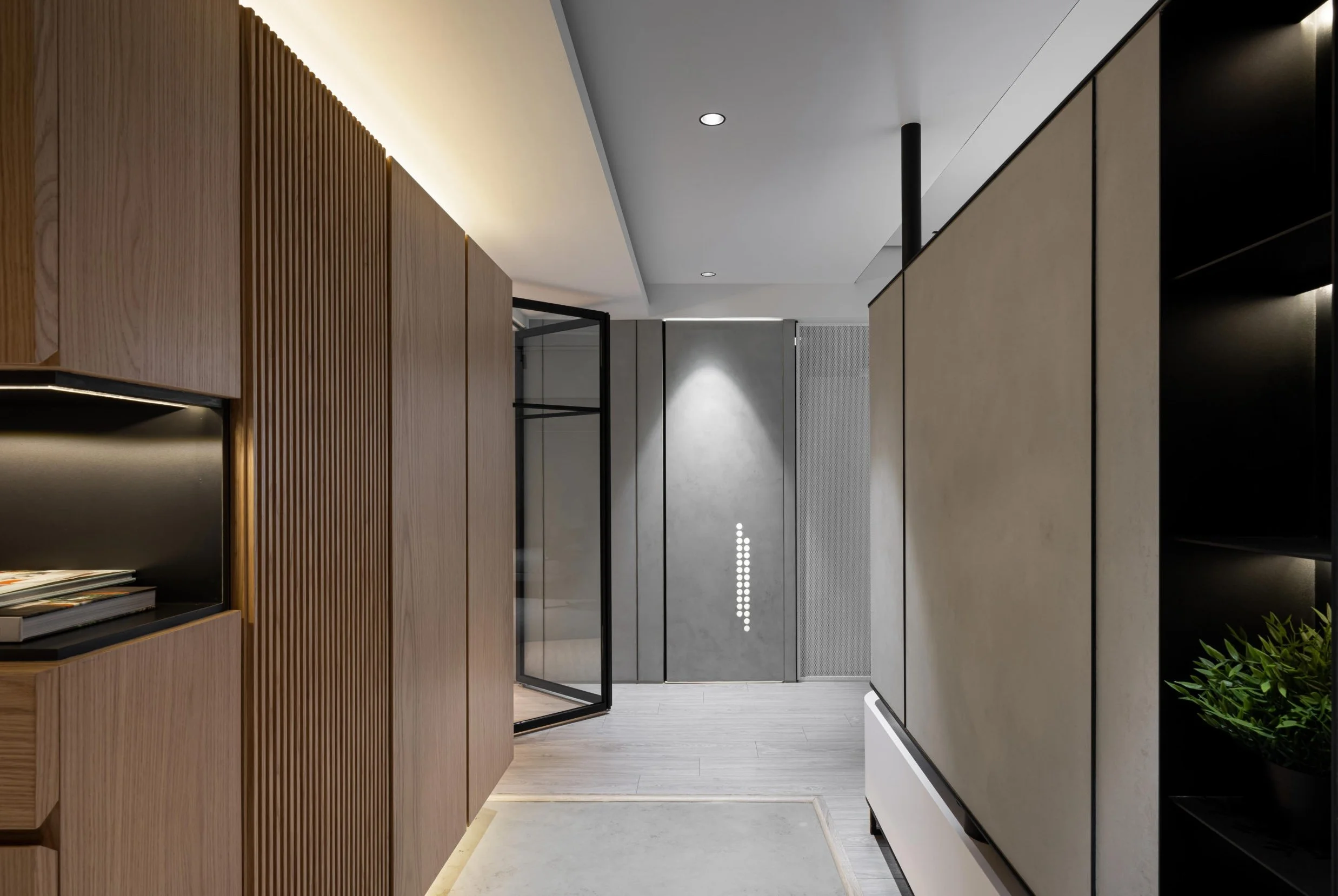 Modern interior with wooden slats on the left, closed elevators on the right, and a corridor with a gray wall and ceiling lights in the background.