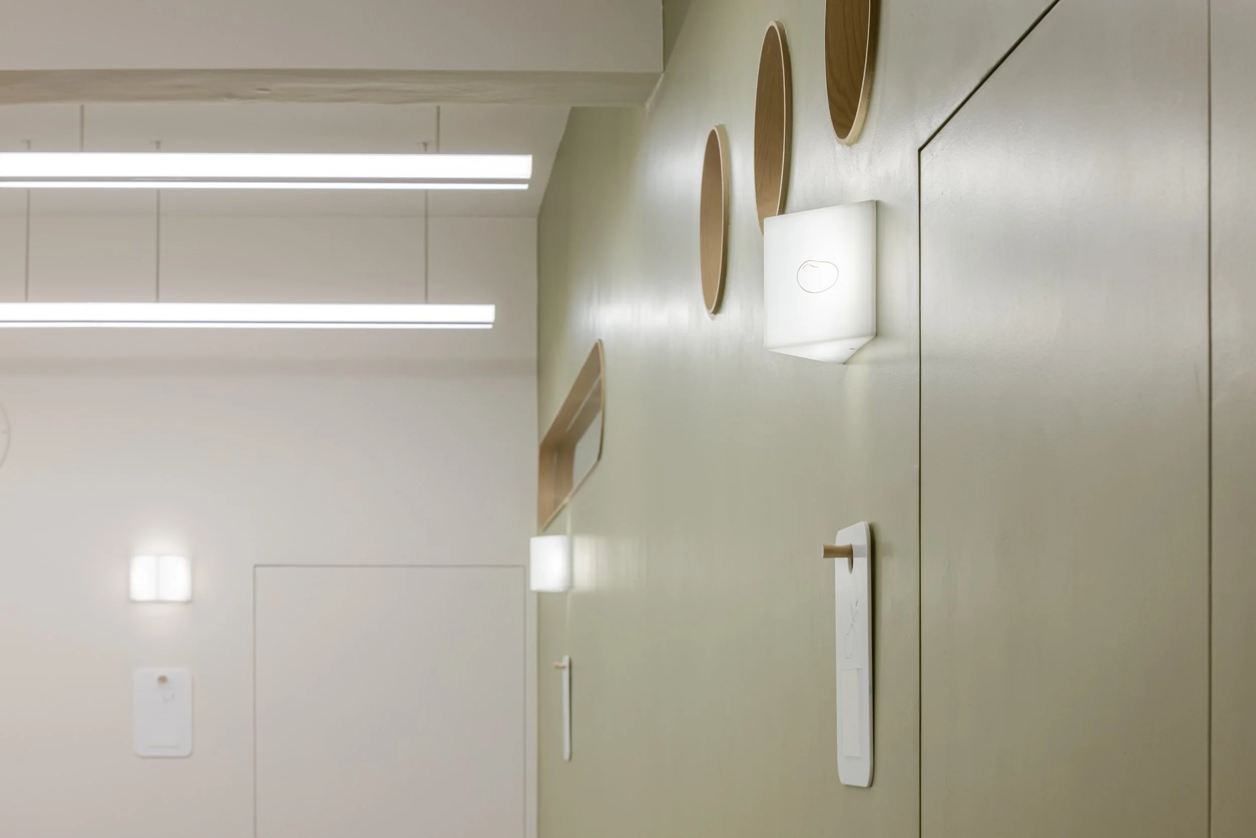 Interior of a modern, minimalist room with a wooden table, round wooden trays, and two built-in wall lights.