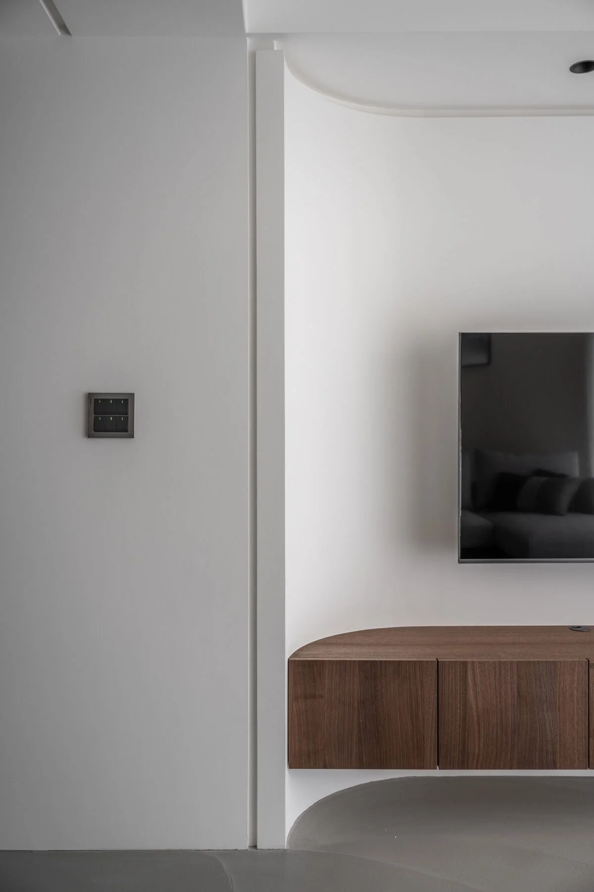 Minimalistic interior with a white wall, a black digital switch, a wall-mounted TV, and a wooden cabinet.