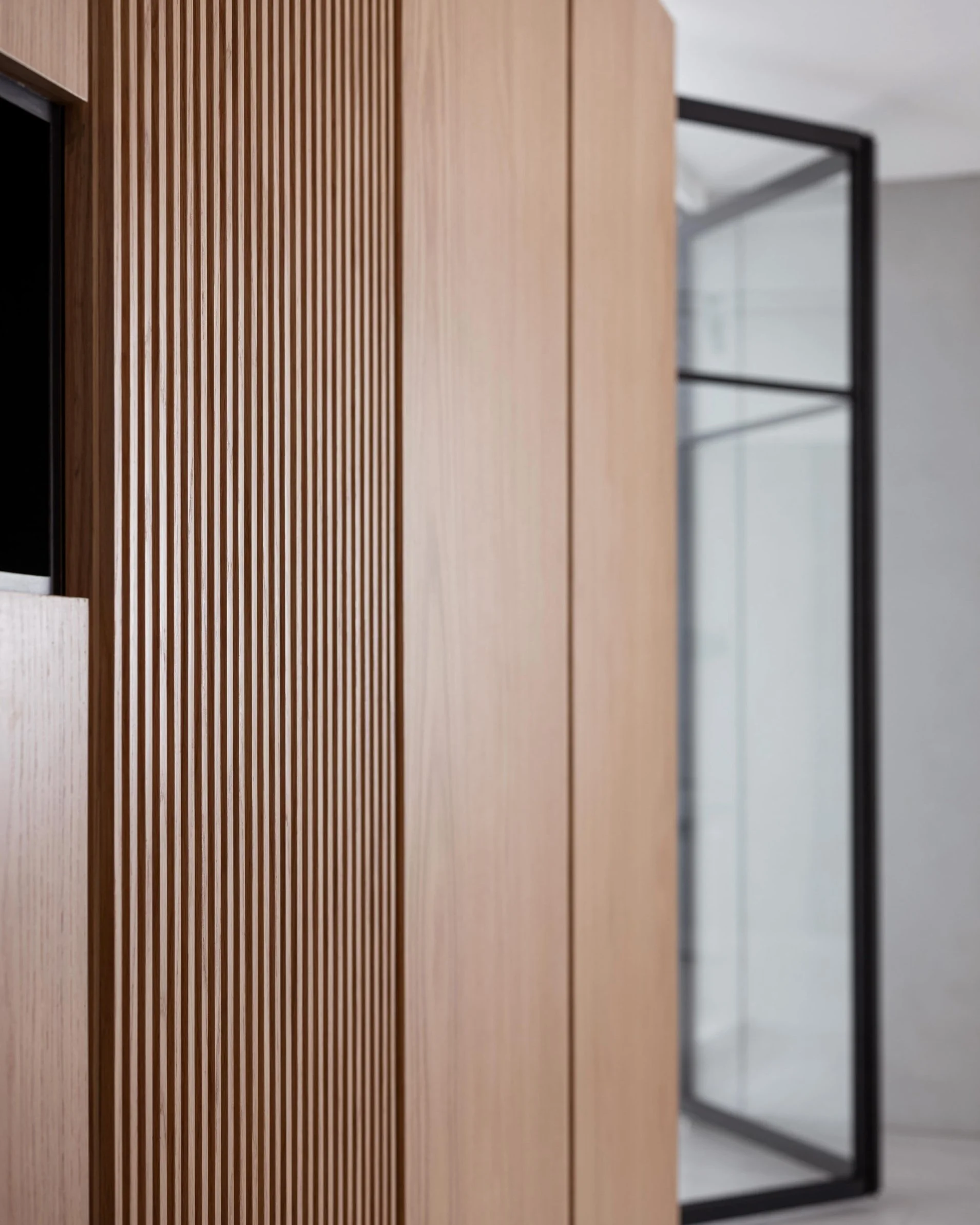 Close-up of a wooden slatted wall with vertical lines and a black metal frame structure in the background.