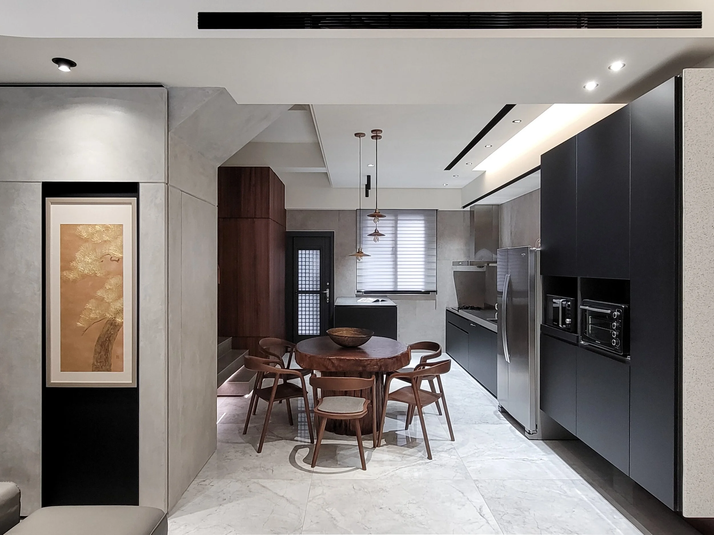 Modern kitchen with dark cabinetry, gray countertops, a round wooden dining table, and wooden chairs in a well-lit space.