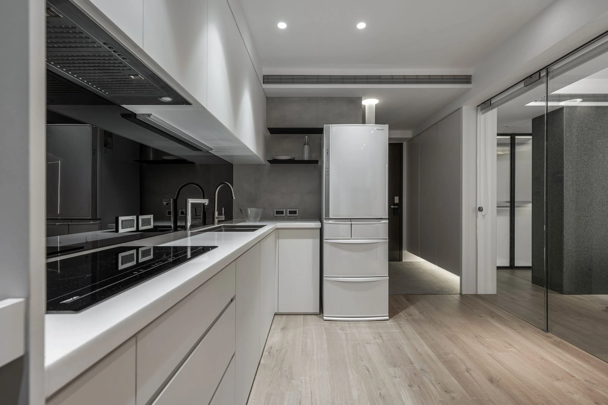 Modern kitchen with white cabinets, black countertop, stainless steel appliances, and wooden flooring.