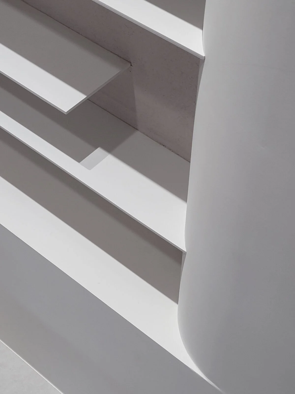 Close-up of a modern, white, minimalist shelving unit with shadowed layers.