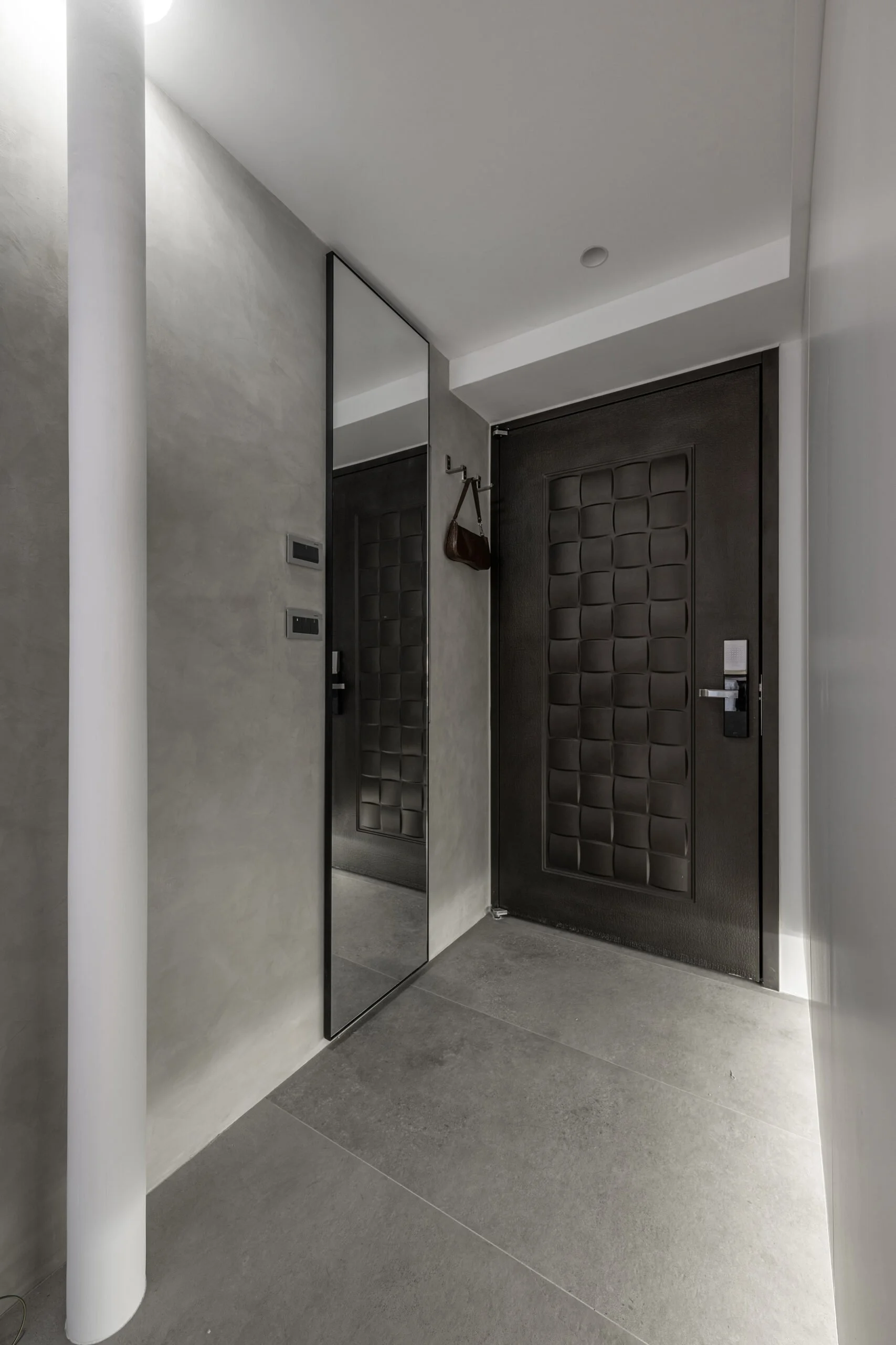 Modern entryway with a large black door that has a grid pattern, a full-length mirror, and a small brown handbag hanging on the wall.
