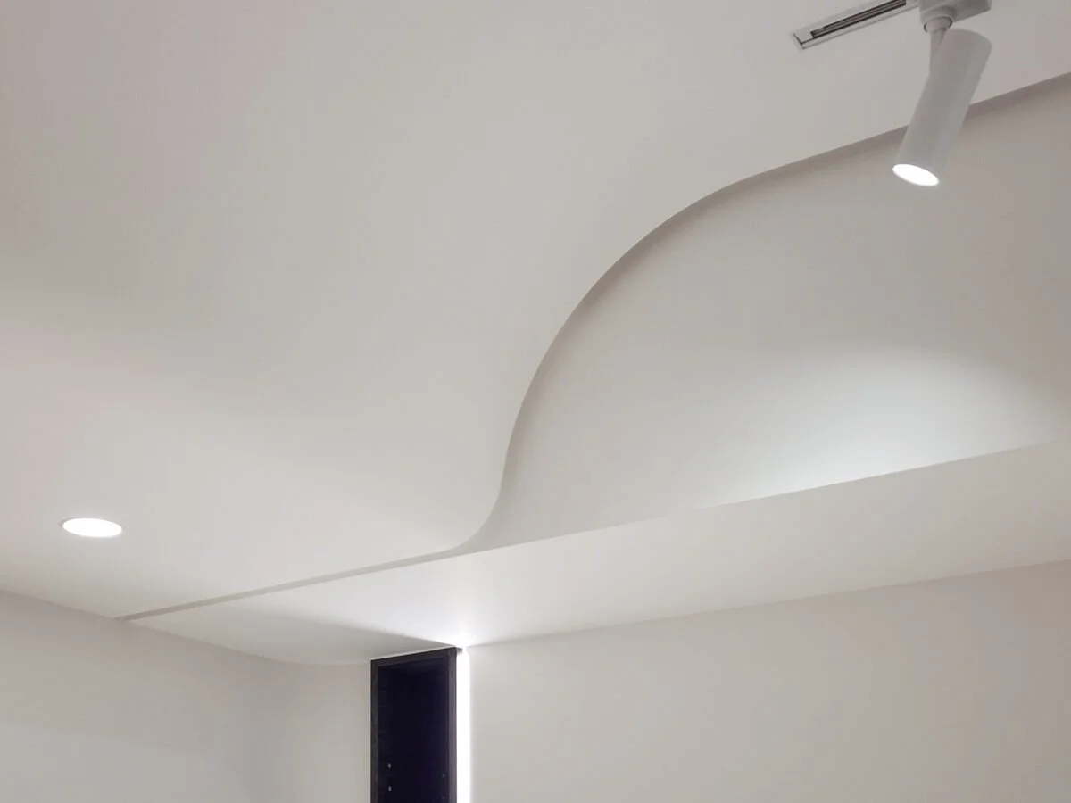 Modern ceiling with recessed and track lighting, metallic black door frame at the top of a white wall, minimalistic and contemporary interior design.