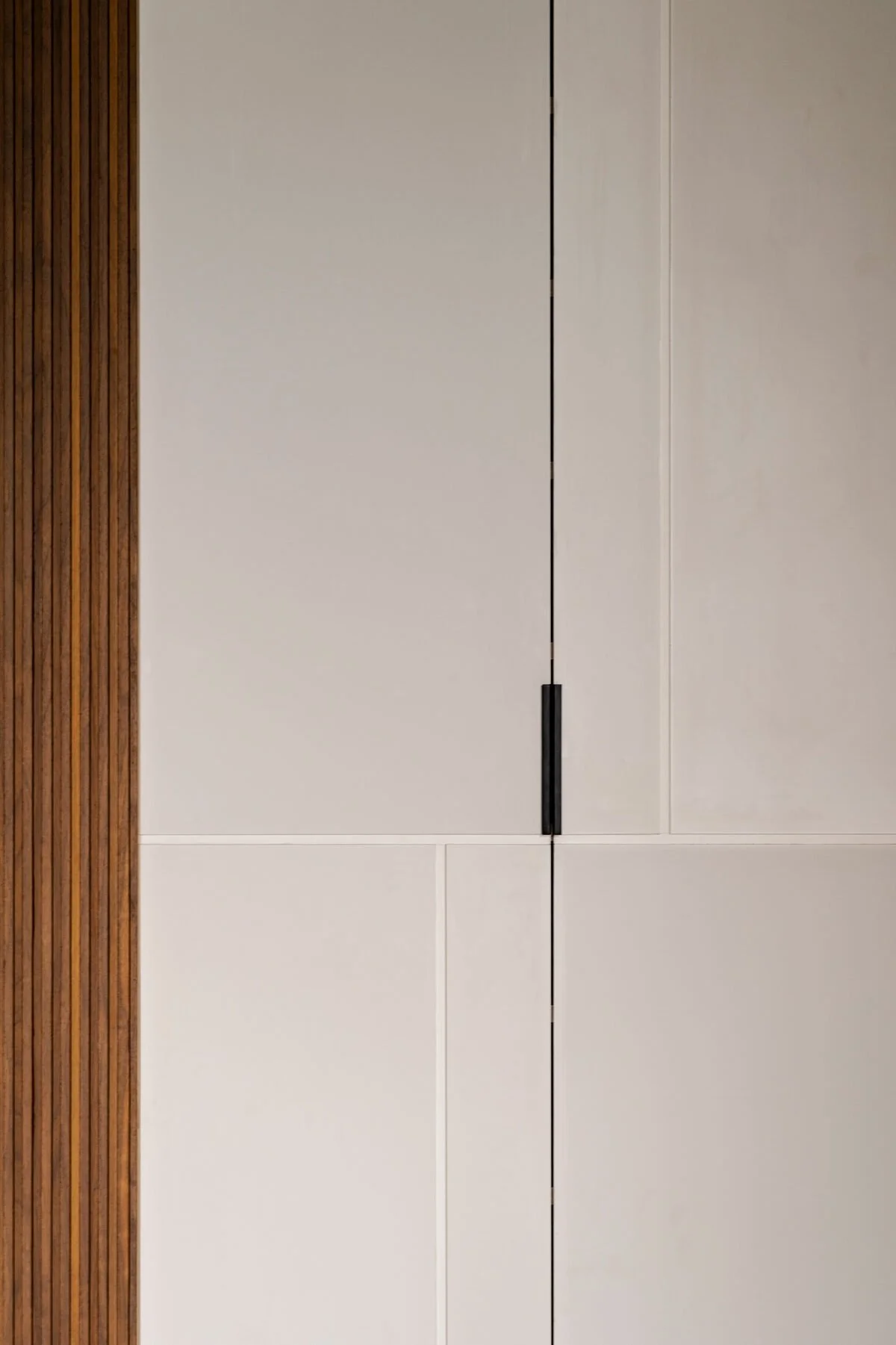 Close-up of a modern white door with a black handle, adjacent to wooden slat wall in interior setting.