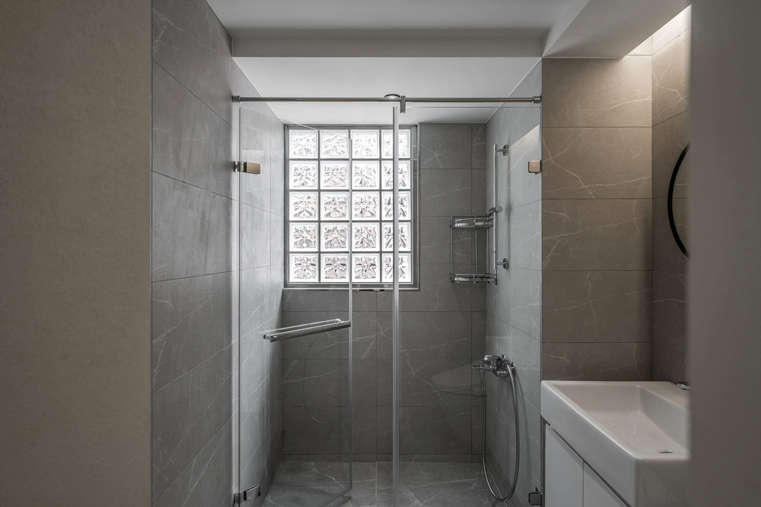 Modern bathroom with gray tiled shower area, glass block window, and shower fixtures.