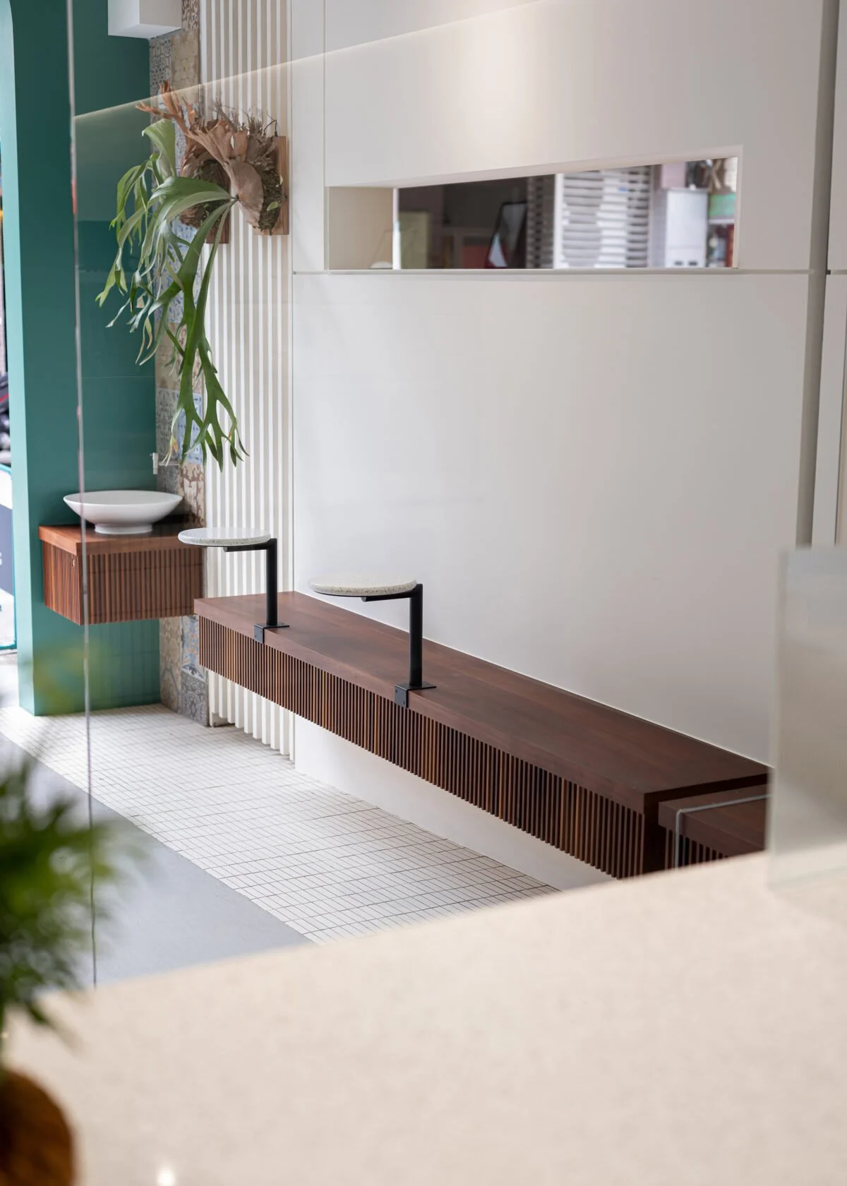 Modern interior design with a wooden bench, a potted plant on a wall-mounted shelf, and a white partition with a cut-out window.