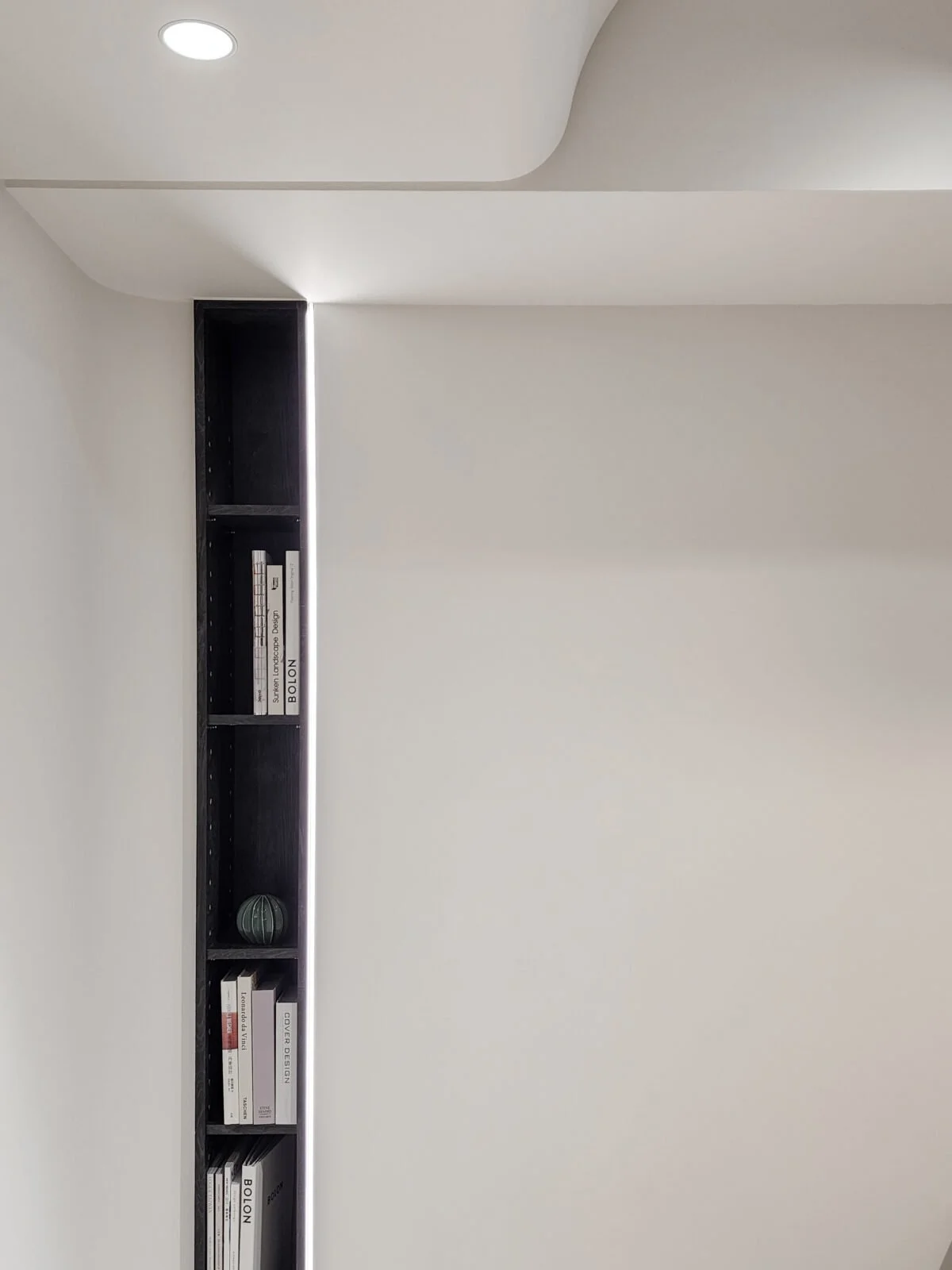 Black bookshelf built into a white wall with books and a small decorative sphere on the shelves.
