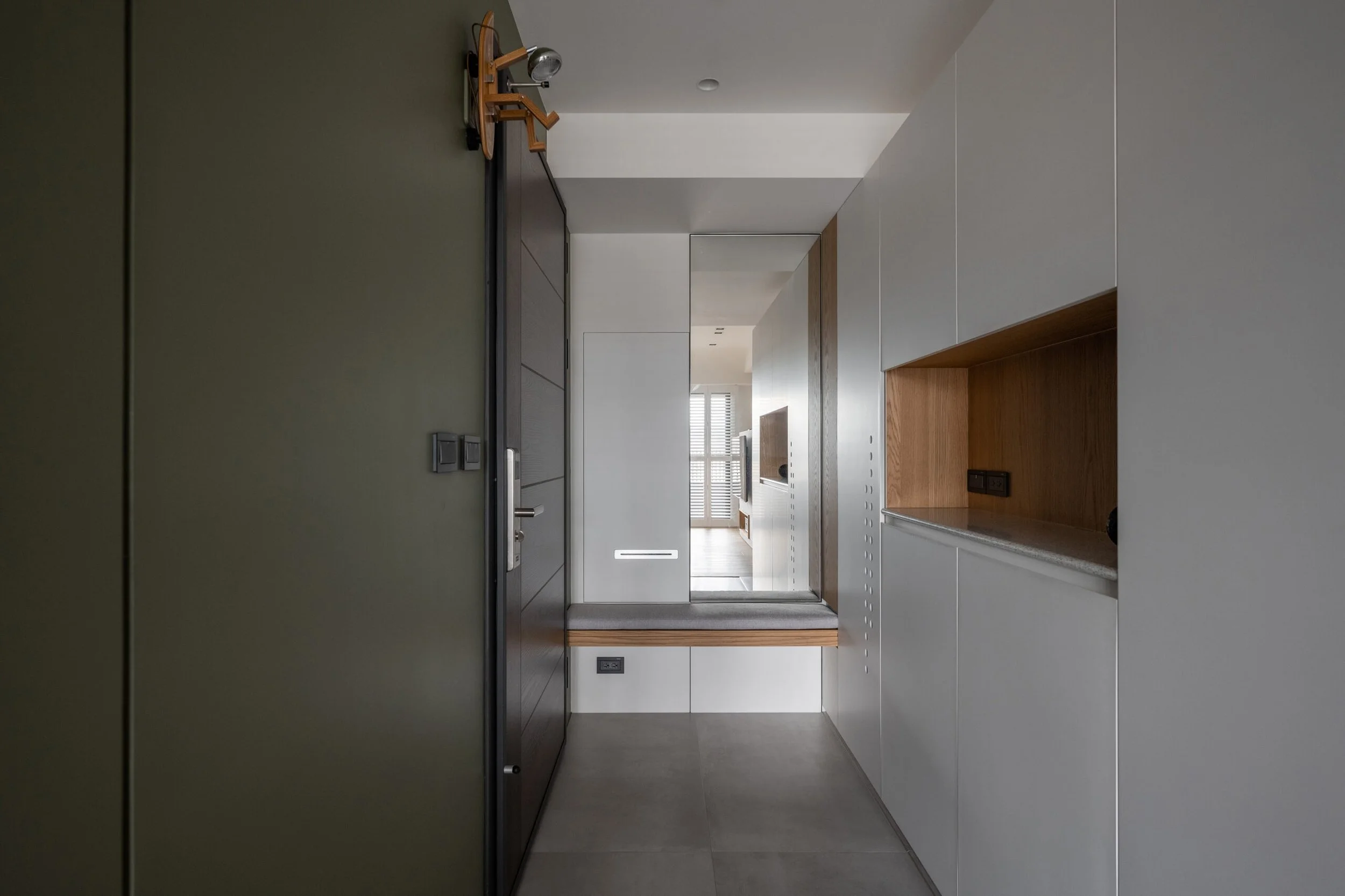 Interior view of a modern hallway with neutral colors, white cabinetry, a wooden accent wall, and a large window with blinds in the background.