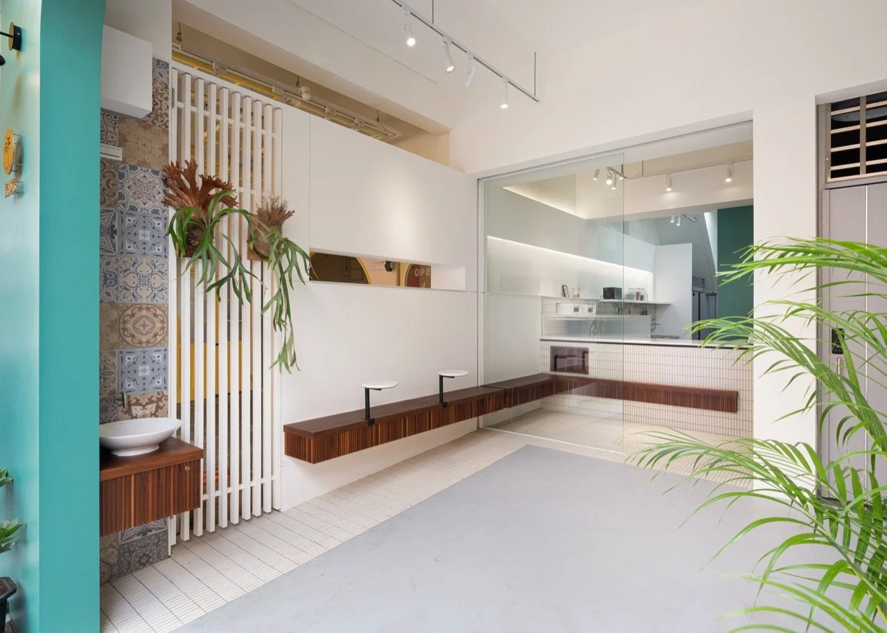 Modern indoor space with a glass partition, wooden benches, green plants, and decorative tile accents.