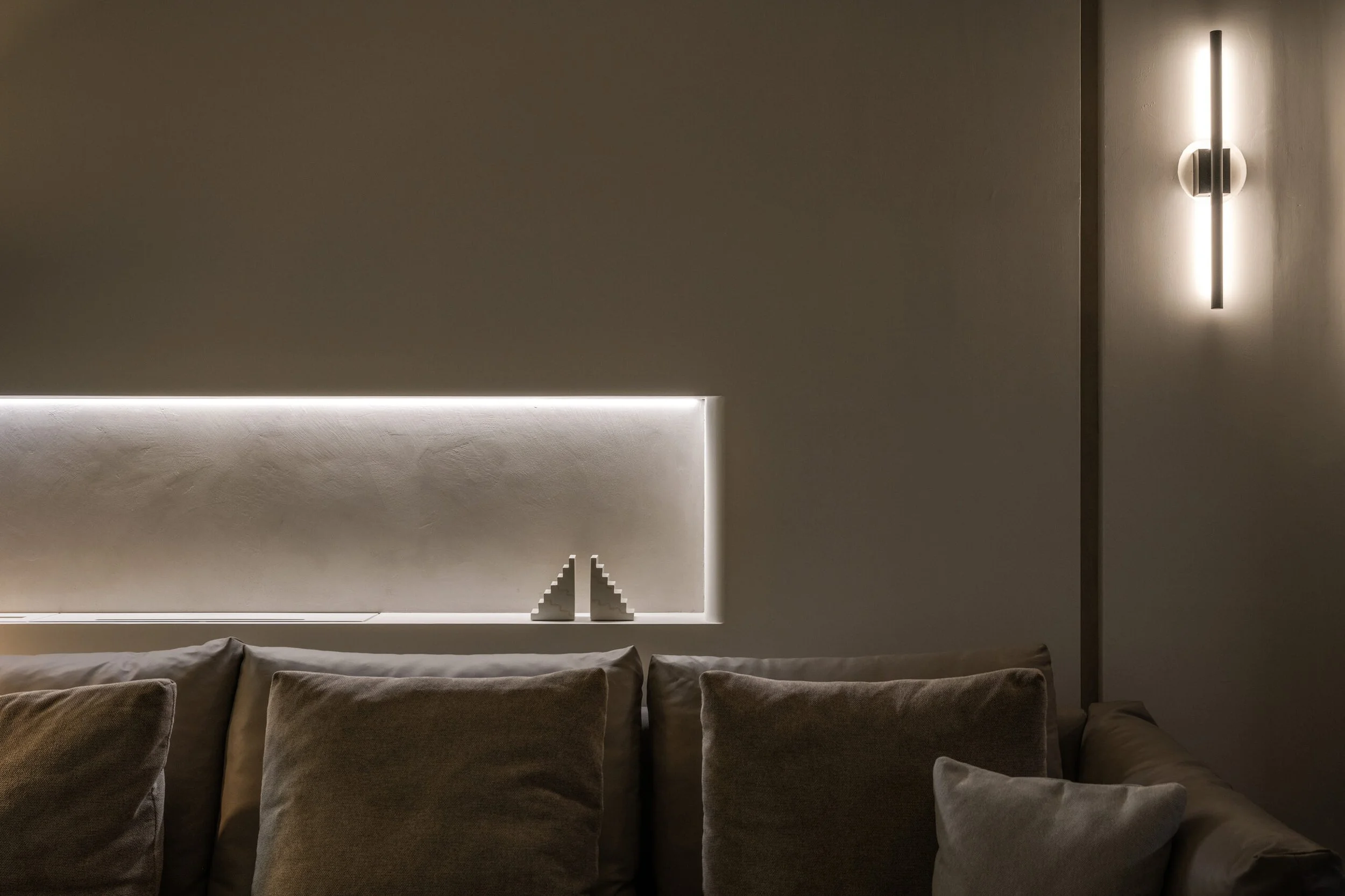 A modern living room wall with minimalist lighting fixtures and a line of brown upholstered chairs.