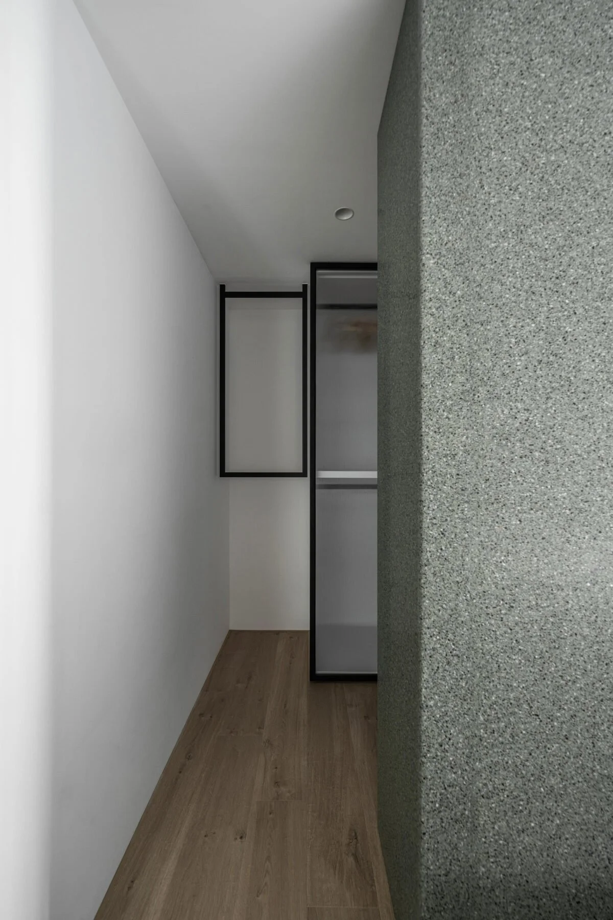 Interior of a modern minimalist room with white walls, wooden floor, black metal frame glass door, and a textured gray stone countertop or partition.
