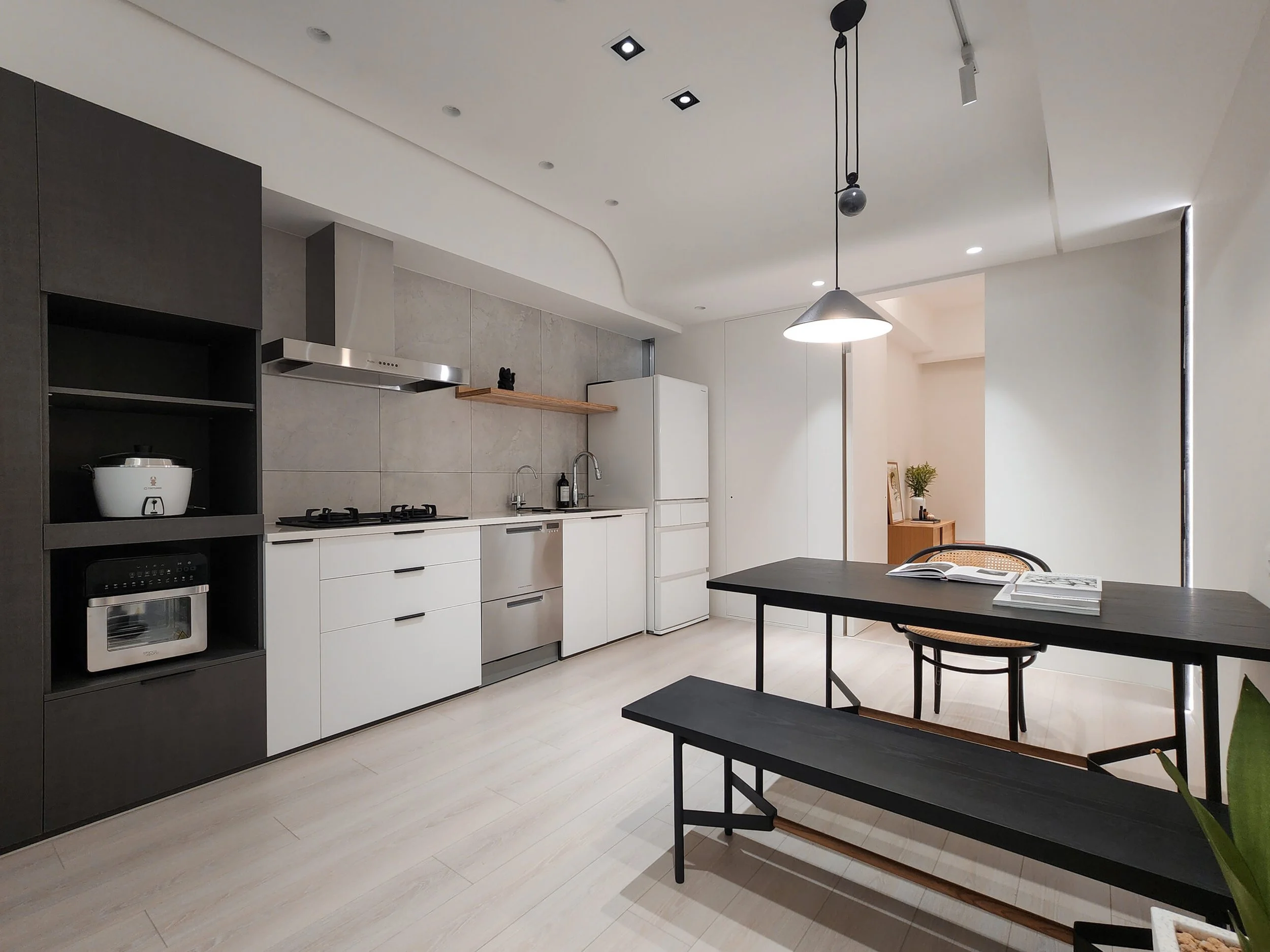 Modern kitchen with white cabinets, stainless steel appliances, gray tile backsplash, black dining table, and hanging pendant lights.