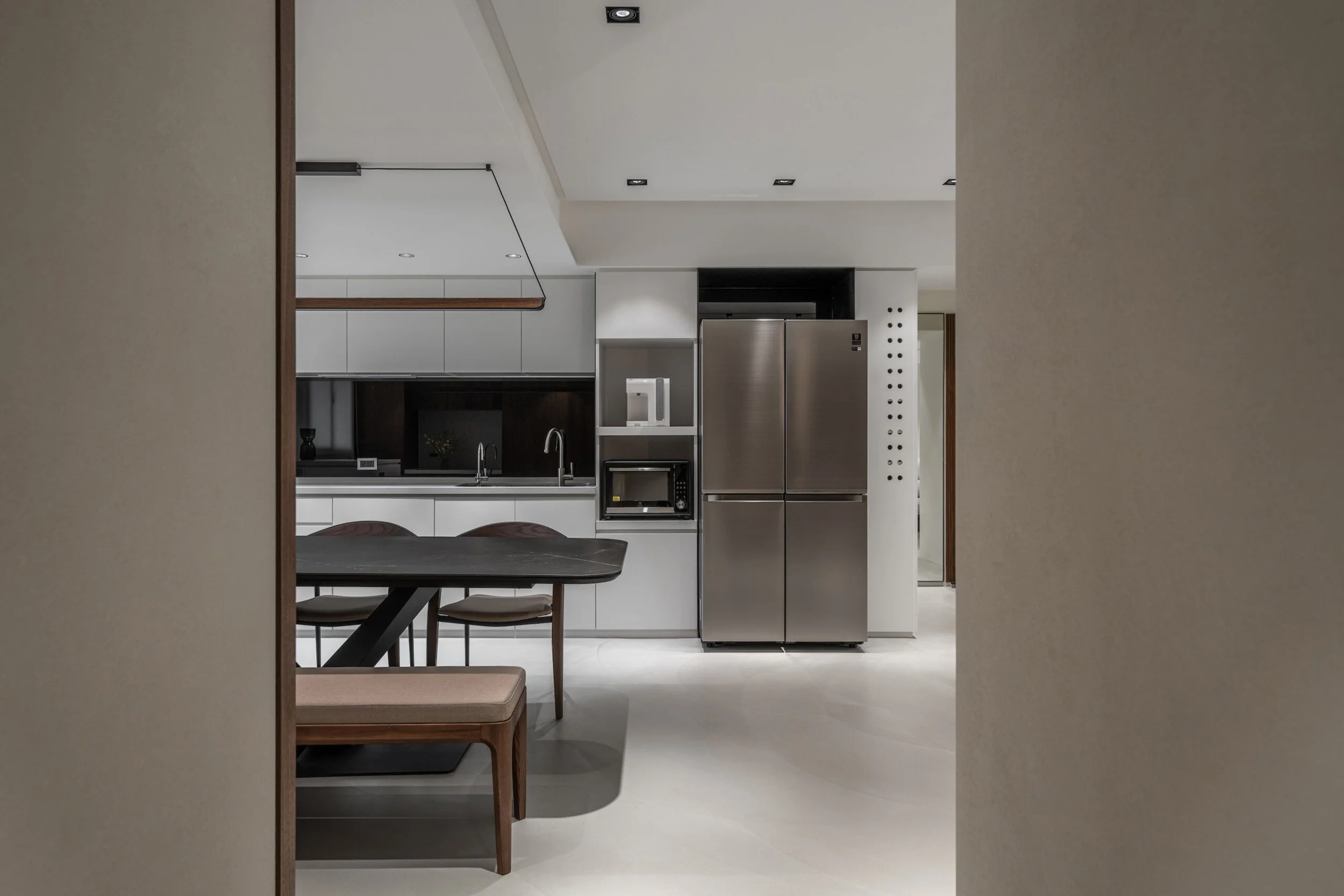 Kitchen view through open doorway showing white cabinetry, stainless steel refrigerator, microwave, and a dark-colored dining table with chairs.