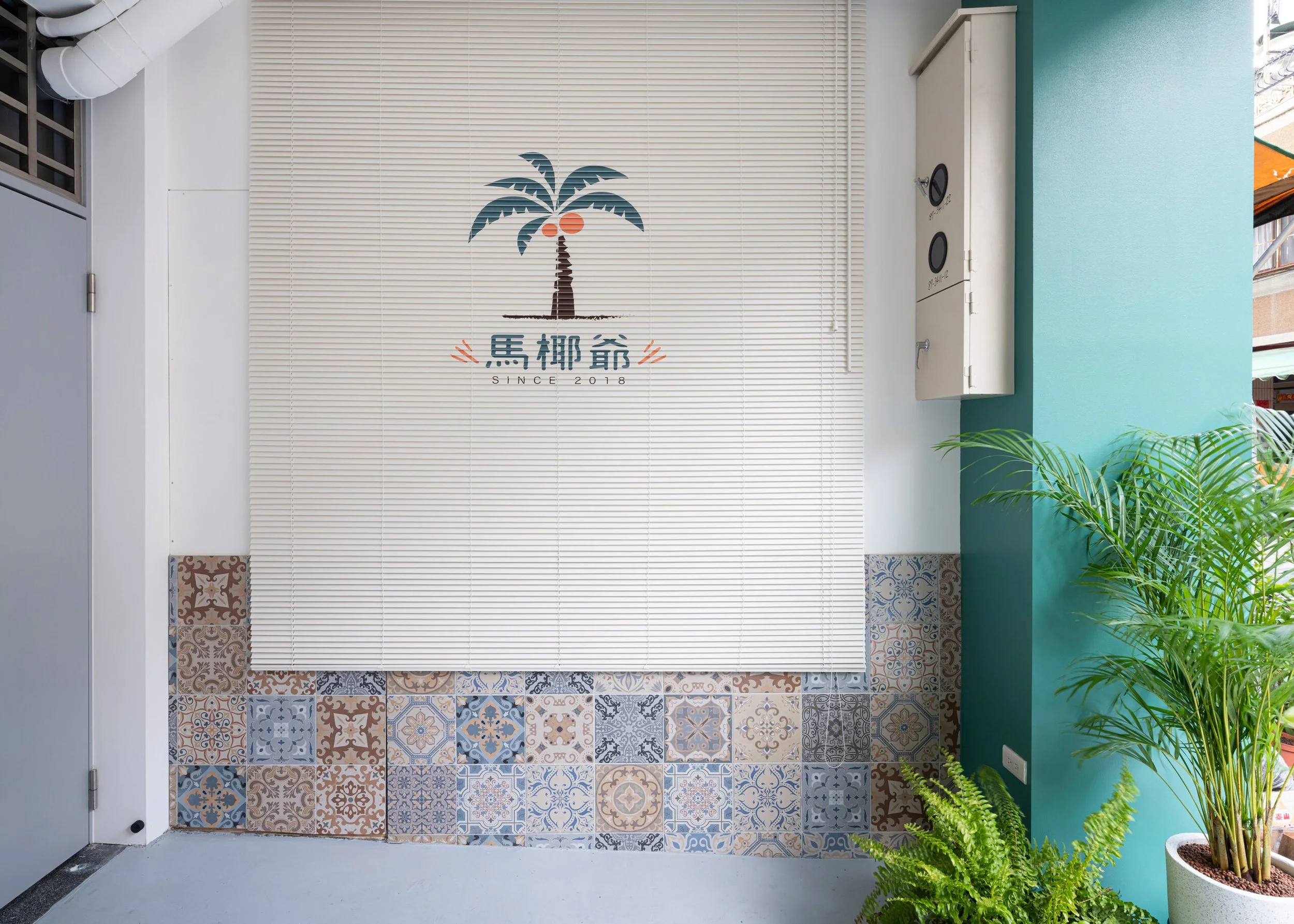 Decorative wall with a palm tree graphic, Chinese characters, and 'Since 2018' text, surrounded by potted plants and colorful patterned tiles at the bottom.