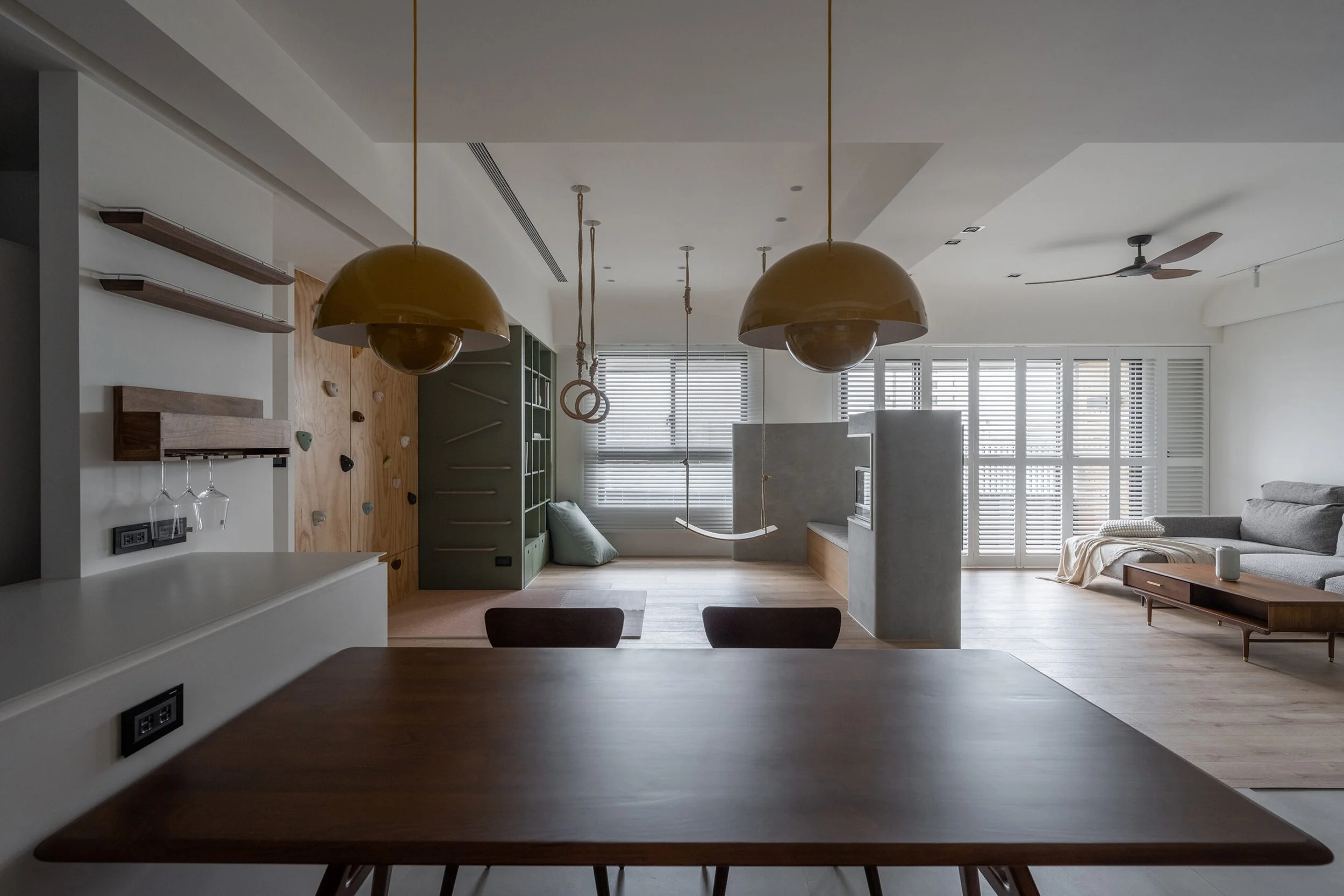 Modern open-concept living space with a ceiling fan, large windows with blinds, a beige sectional sofa, and a wooden coffee table.