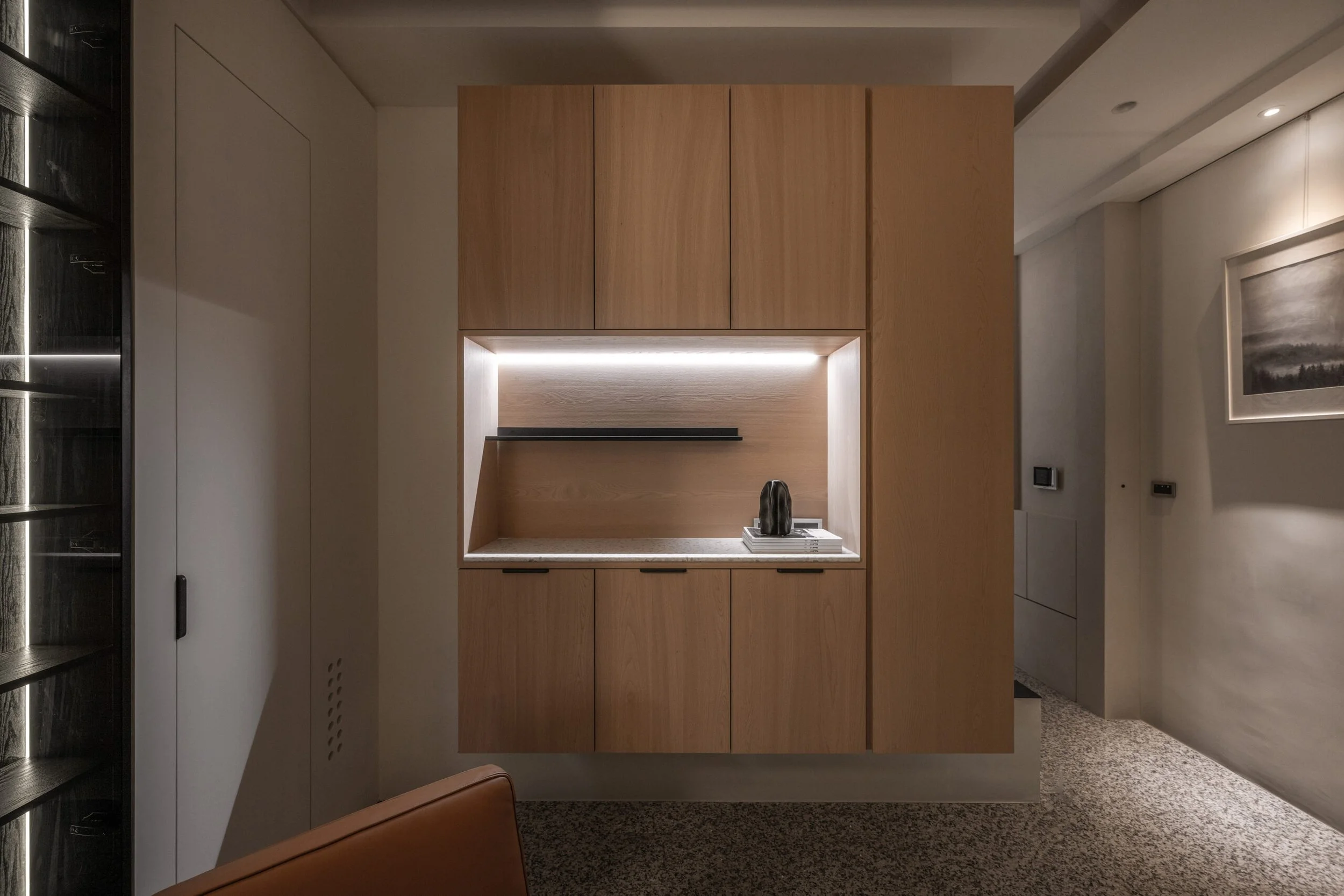 Modern kitchen wall with wooden cabinets, a built-in open shelf with black objects, and a wall-mounted frame with landscape art.