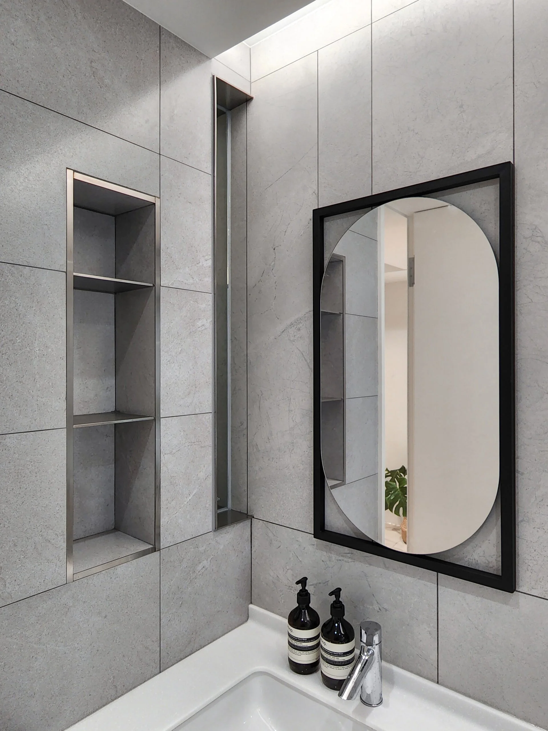 Bathroom sink with three black bottles, a silver faucet, and a round mirror on a tiled wall.