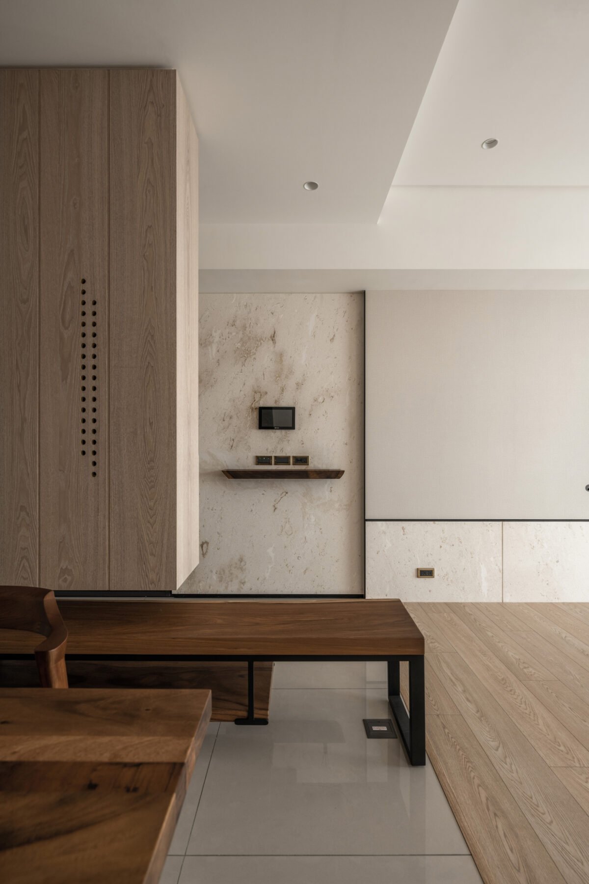 Modern living room with wooden furniture, a textured wall, built-in small TV, and decorative shelves.