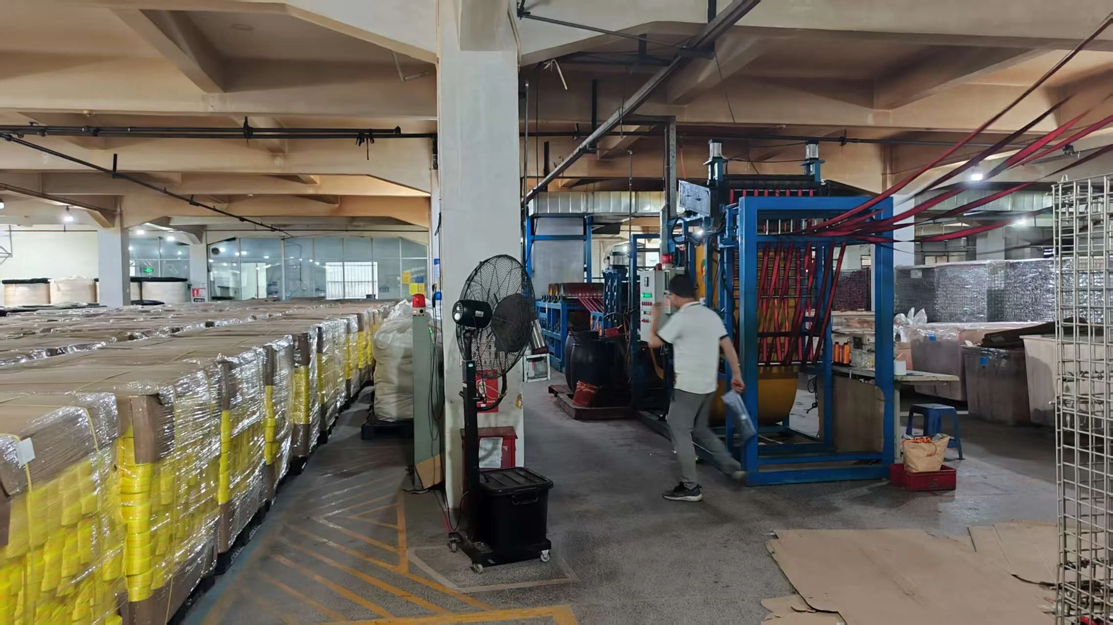 Warehouse interior with packed large items wrapped in plastic, machinery, and a worker.