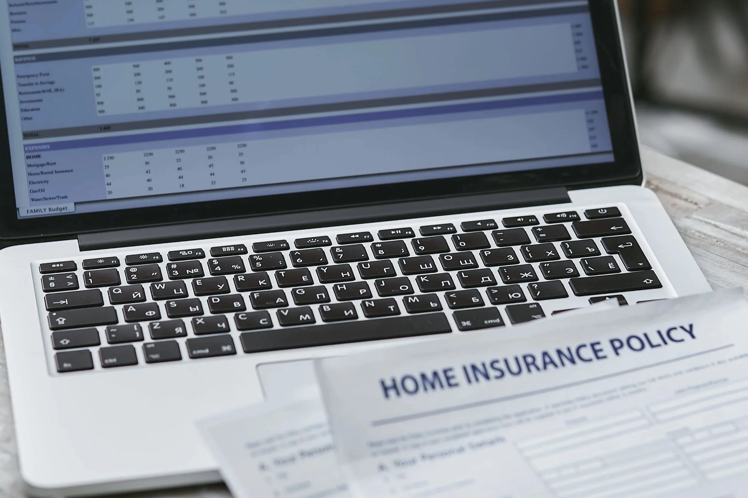 Close-up of a laptop screen displaying a home insurance policy document and a partial view of the keyboard on a wooden surface.
