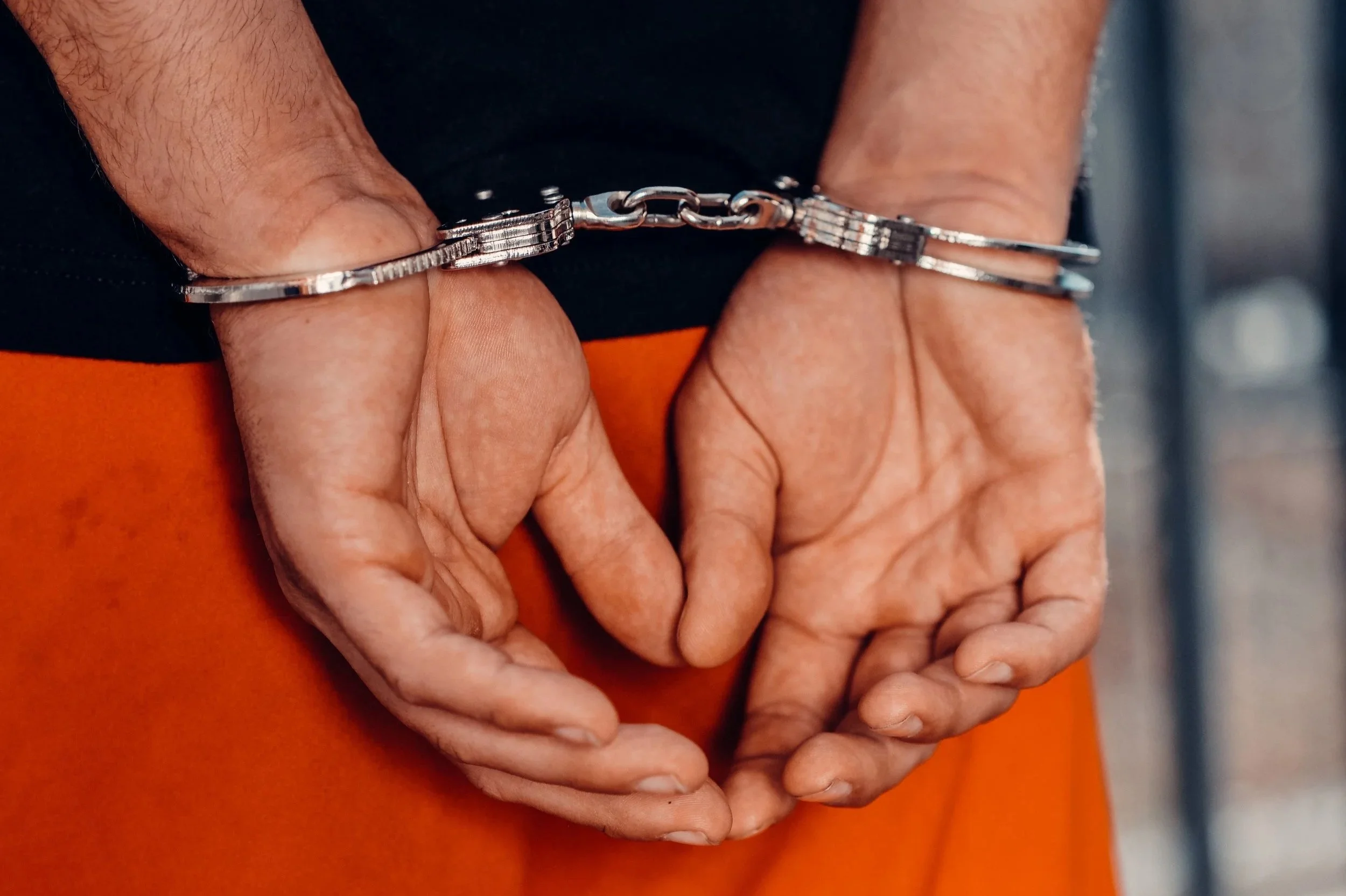 Close-up of a person holding their hands together, with handcuffs around their wrists.