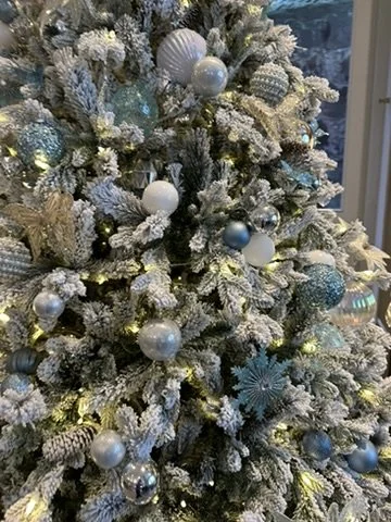 Frosted Christmas tree decorated with white, blue, and silver ornaments and lights.