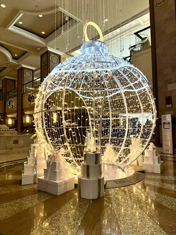 Large globe-shaped bauble with decorative lights, placed in the Langham Hotel lobby surrounded by white presents.