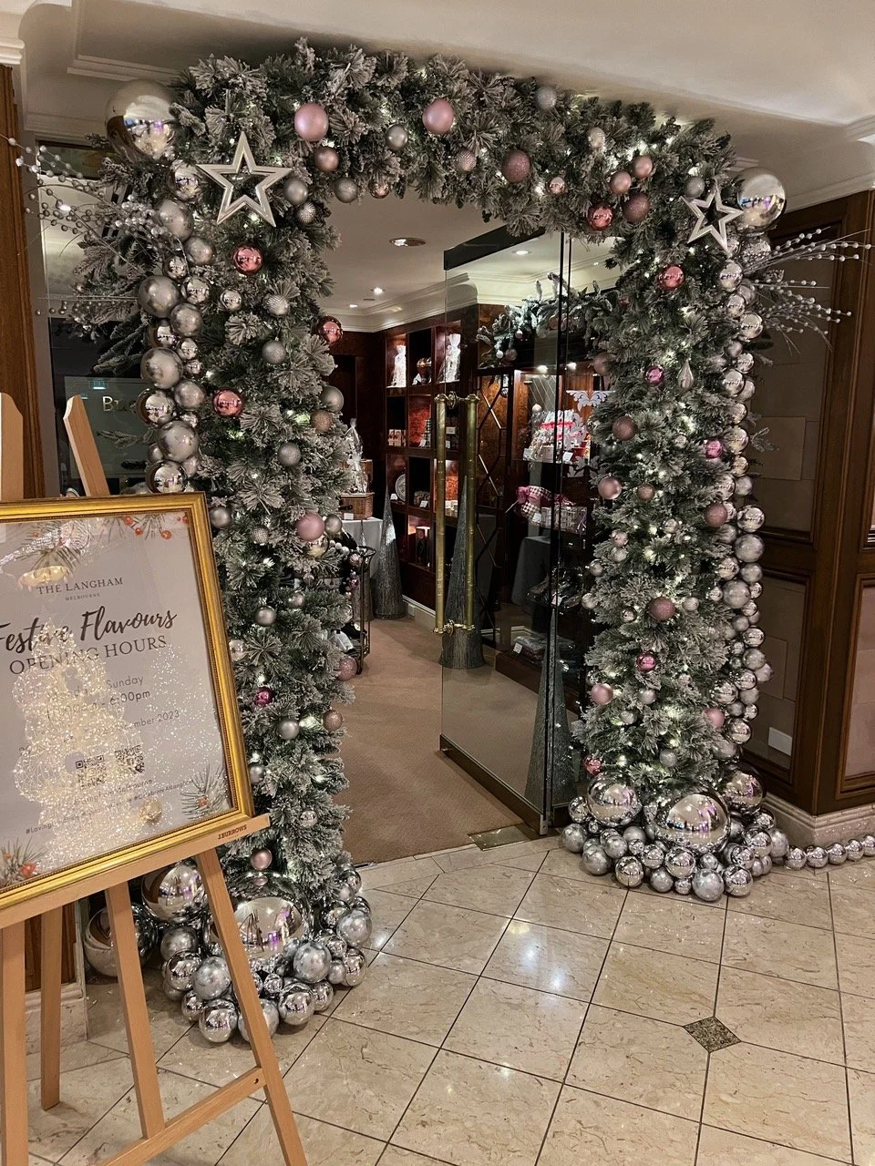 Christmas decorated archway with silver and pink ornaments, star and snowflake accents, leading into a room with wooden shelves and a signboard on an easel.