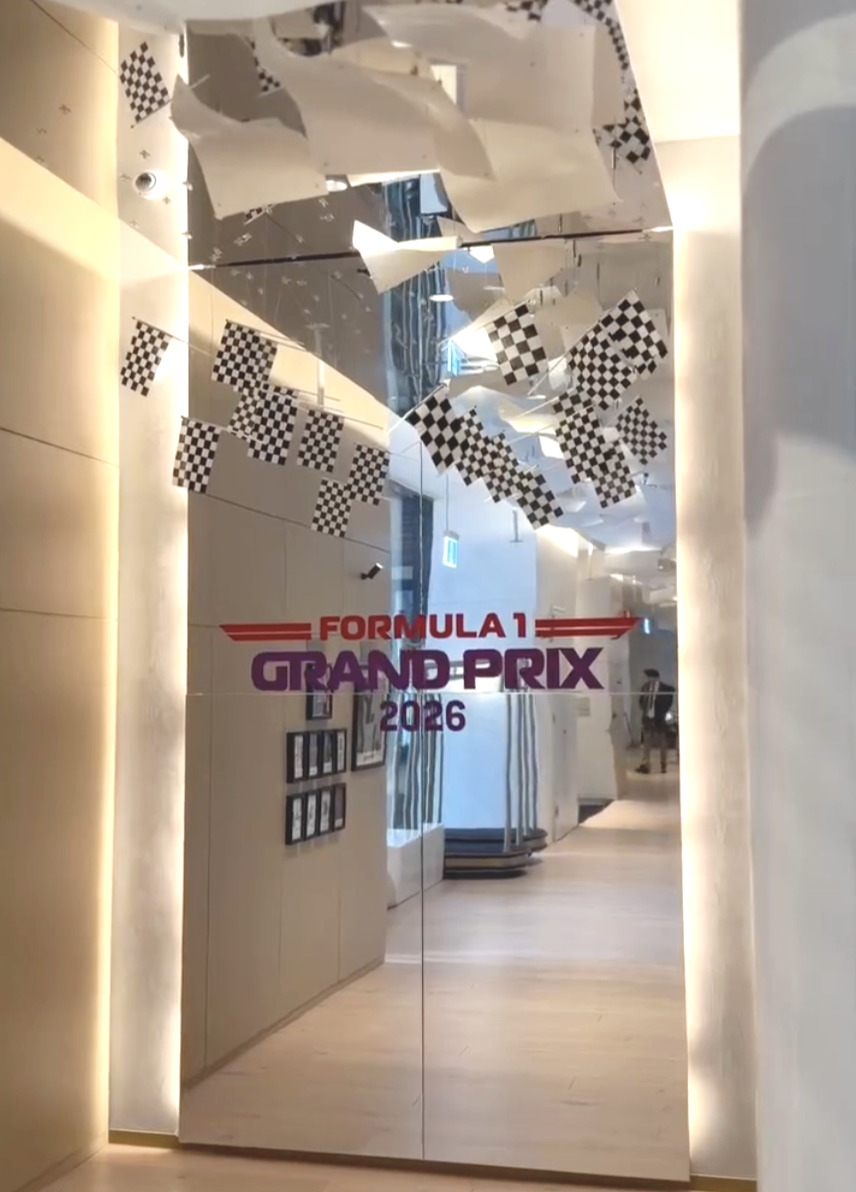 Mirror reflection with Formula 1 Grand Prix 2026 signage, black and white checkered flags, and decorative hanging pieces.