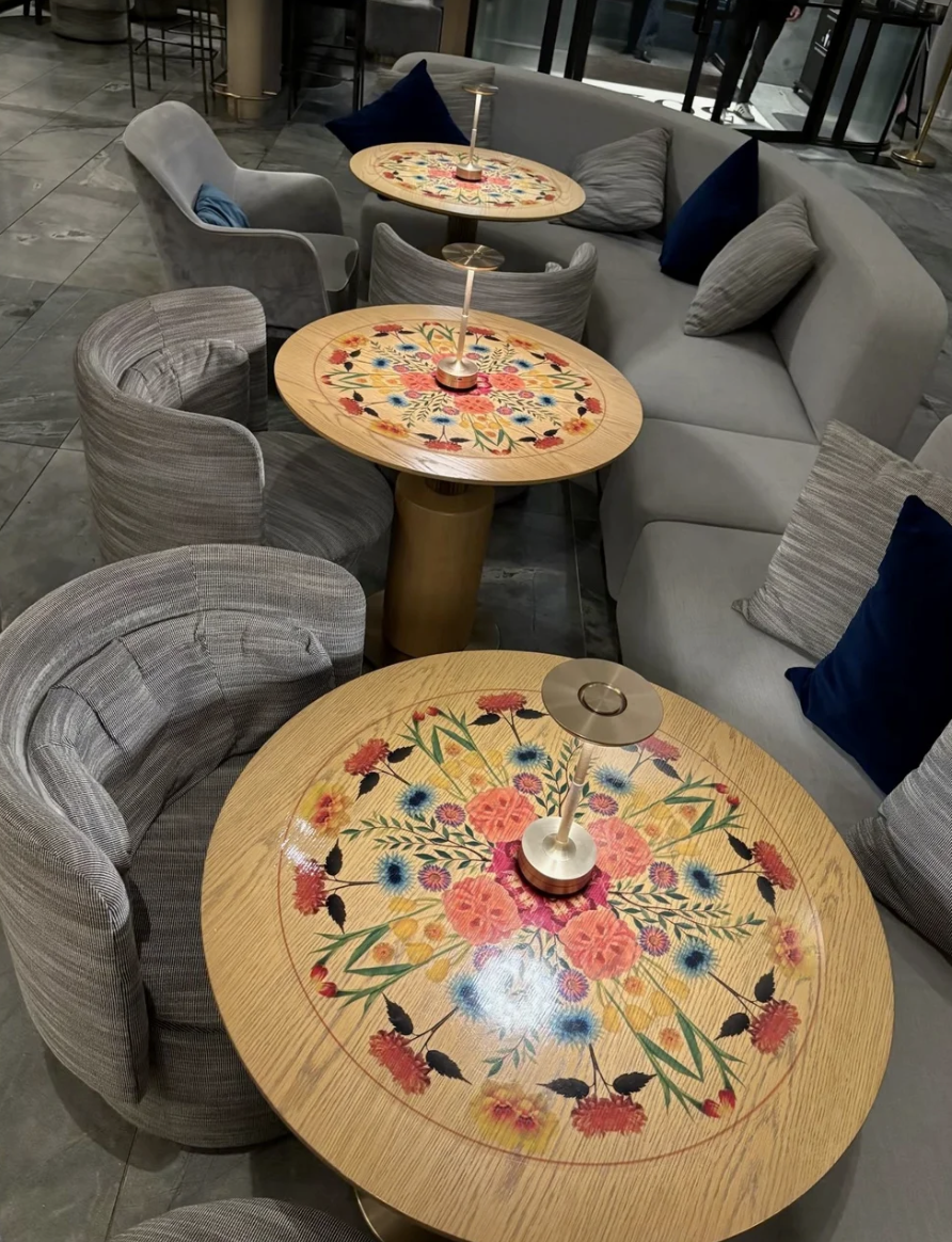 Three round tables with kaleidoscope flower design on the tops - designed by Cindy Lee at TELIPOK - surrounded by various chairs and a sofa with throw pillows, in a modern indoor setting.